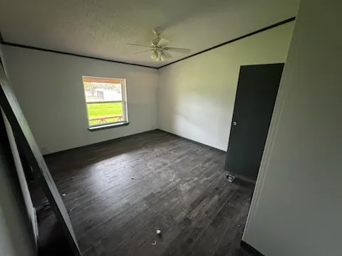 Empty room featuring dark wood-style flooring, a textured ceiling, and a ceiling fan