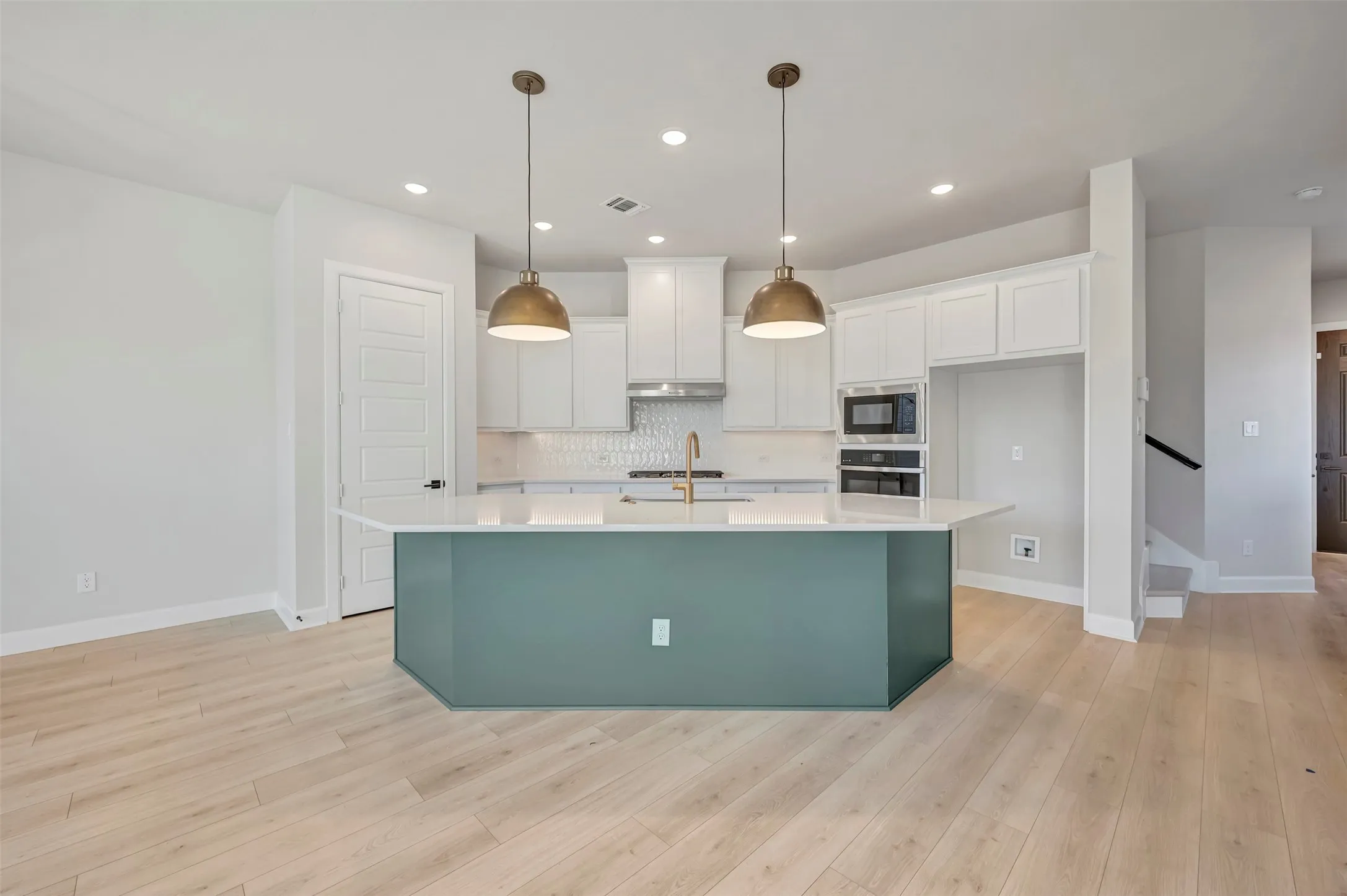 Kitchen with an island with sink, stainless steel appliances, light wood-style floors, pendant lighting, and two tone cabinetry