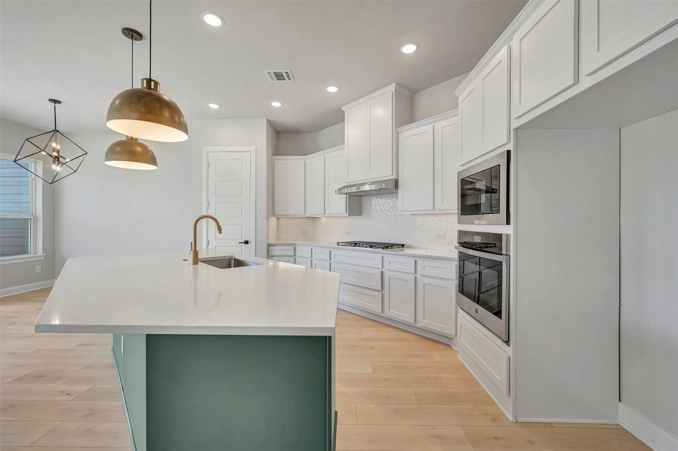 Dual tone kitchen with an island with sink, stainless steel appliances, tasteful backsplash, light wood finished floors, and light stone countertops