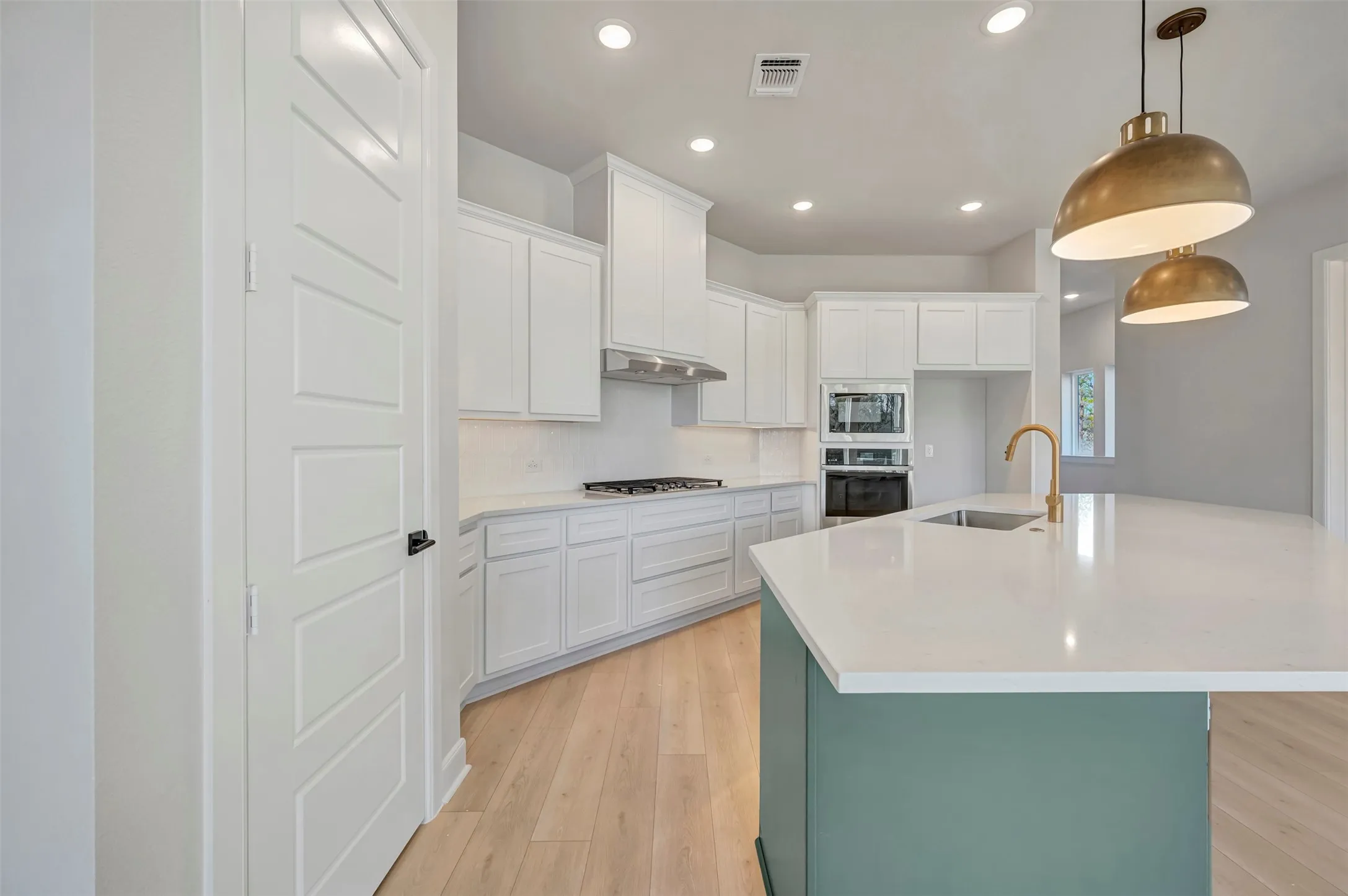 Dual tone kitchen featuring a center island with sink, light wood-style flooring, stainless steel appliances, hanging light fixtures, and two tone cabinets