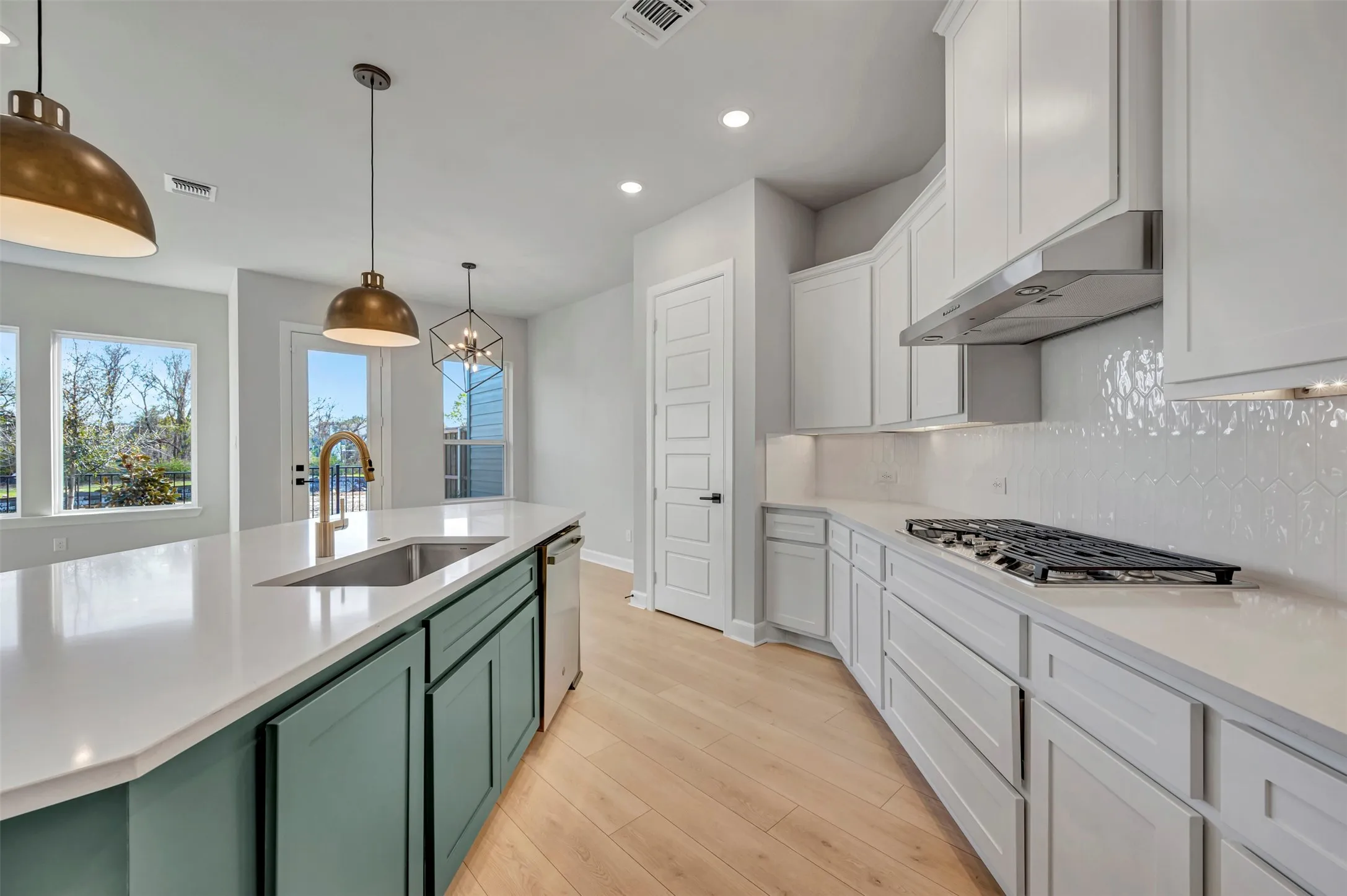 Kitchen featuring backsplash, dual tone cabinetry, light wood-style flooring, decorative light fixtures, and stainless steel appliances