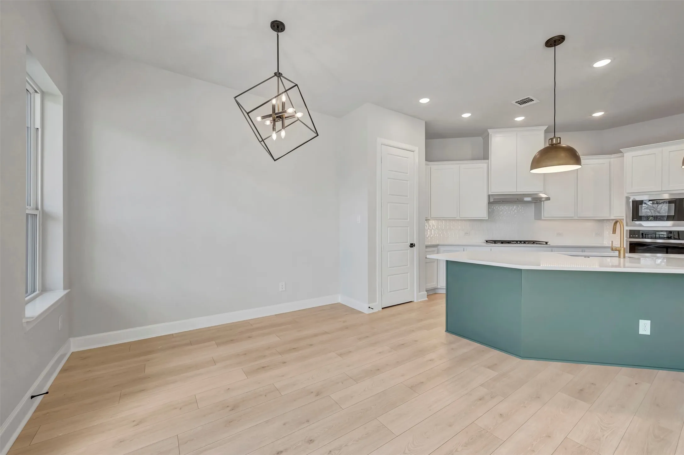 Kitchen with white cabinetry, hanging lights, light wood-type flooring, and stainless steel appliances
