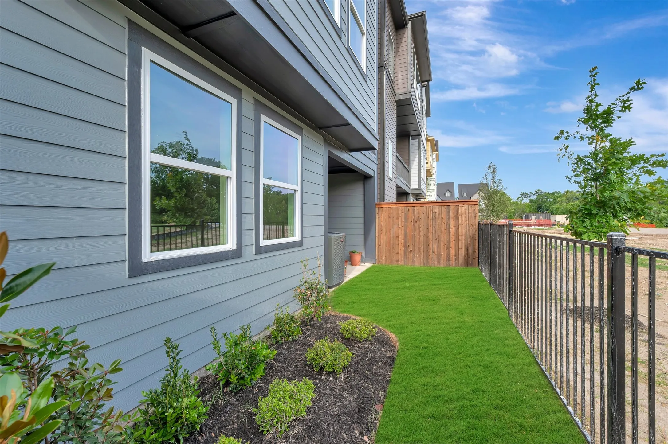 Manicured green lawn with a black metal fence and privacy wood fencing