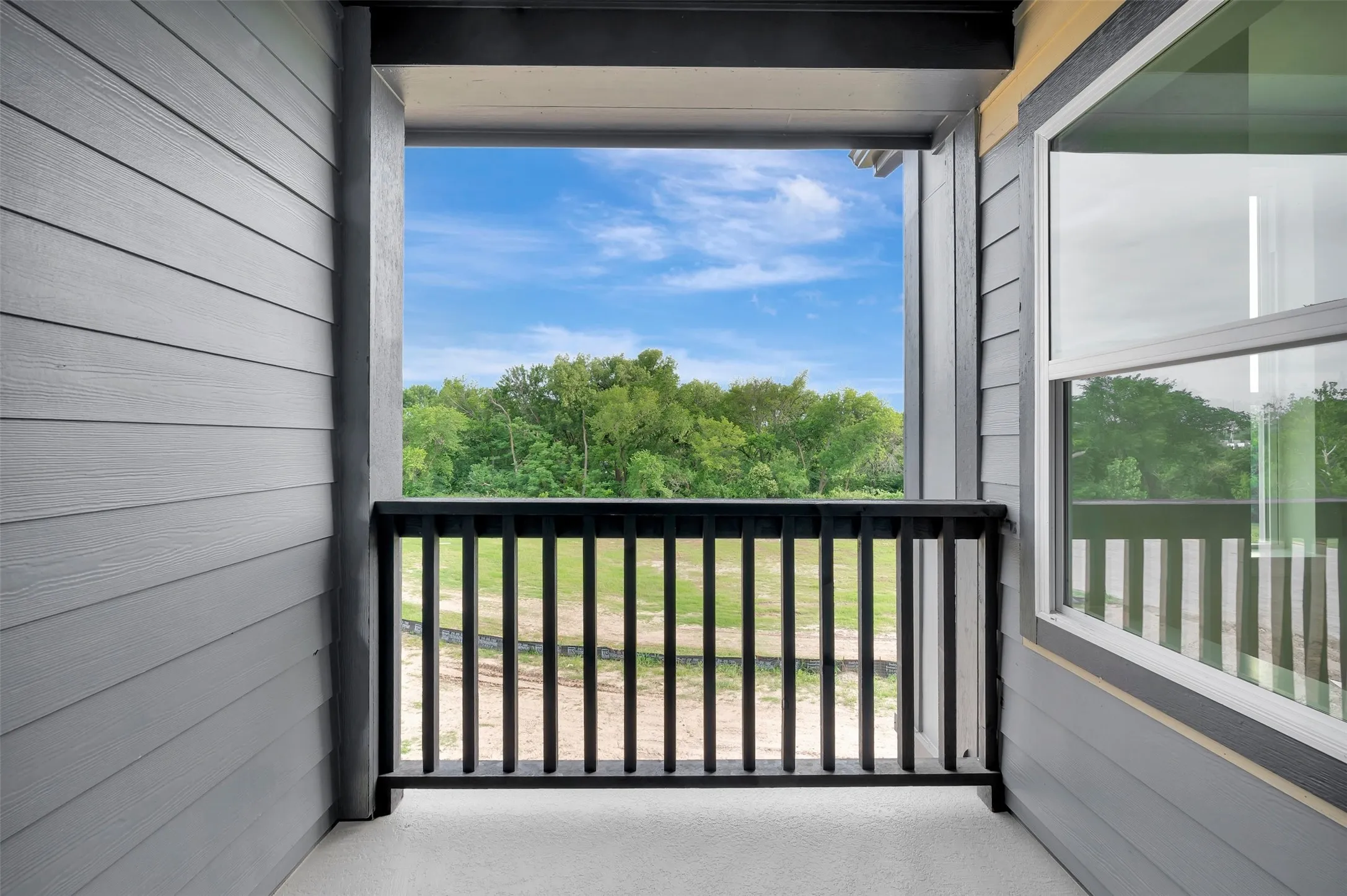 Private balcony featuring gray horizontal siding, black vertical railings, and a clear expanse of sky and distant trees
