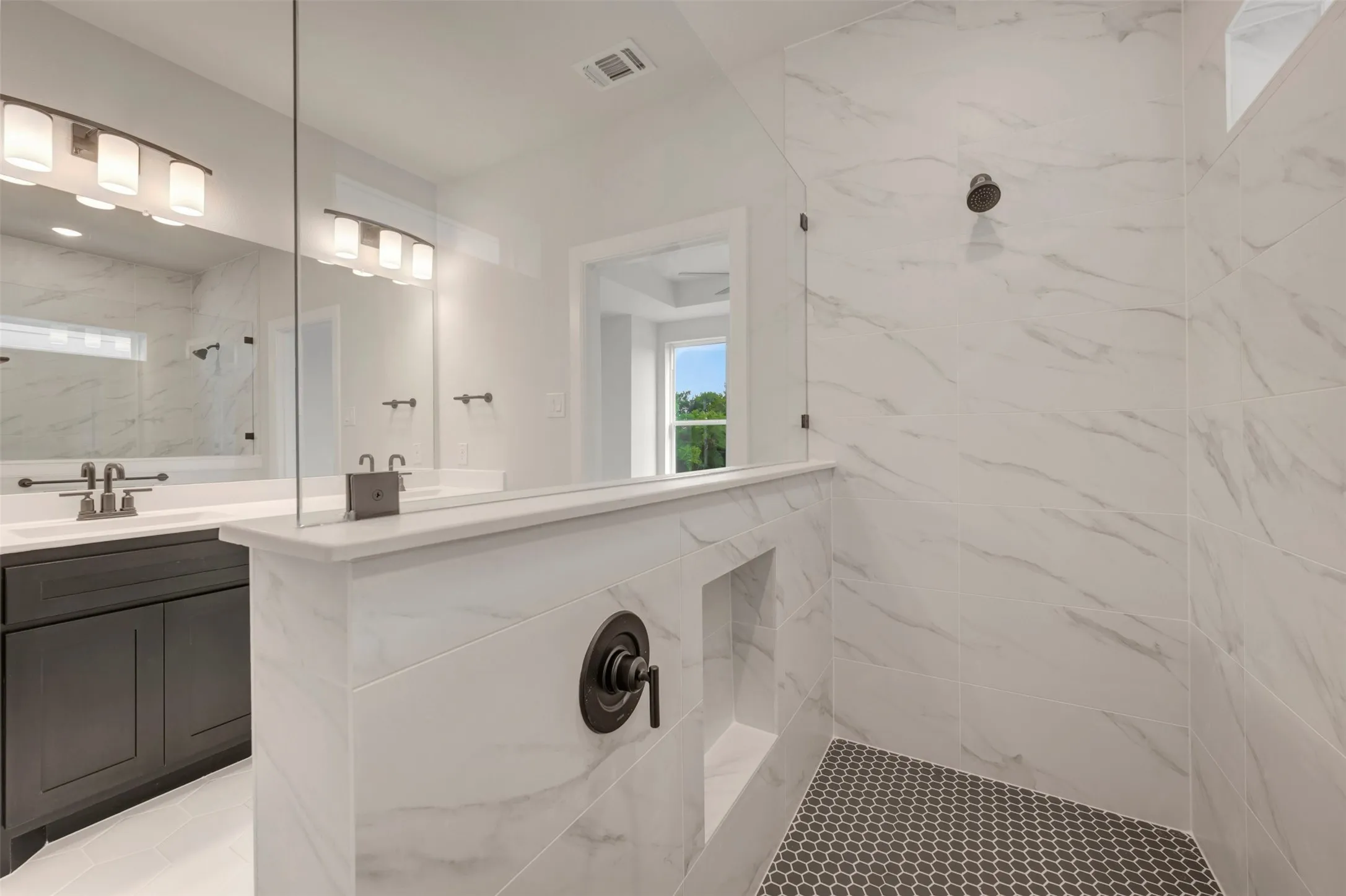 Walk-in shower featuring gray penny tile flooring, marble-look wall tiling, and matte black fixtures