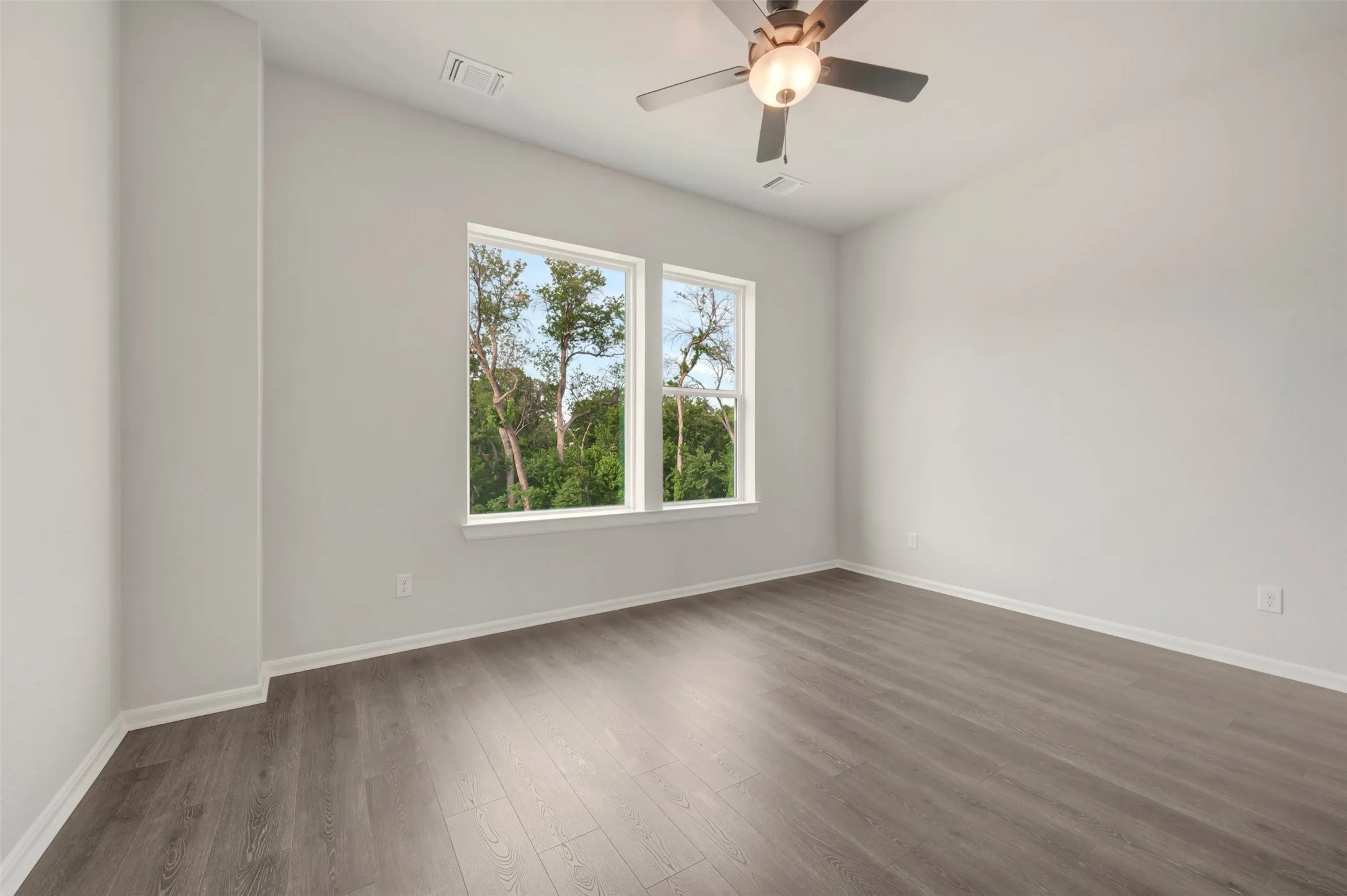 Spacious room featuring multiple windows, wood-finish flooring, a ceiling fan with light fixture, white walls, and white baseboards