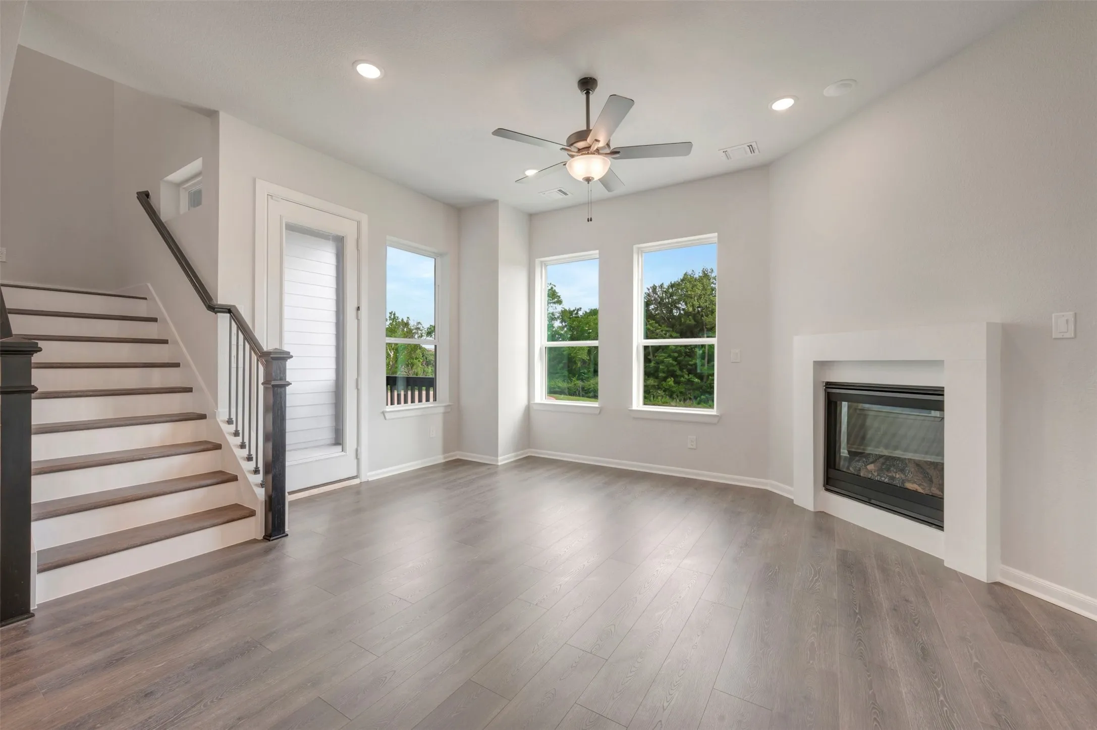 Living area featuring wood-finish flooring, a contemporary fireplace with a white surround, and three large windows
