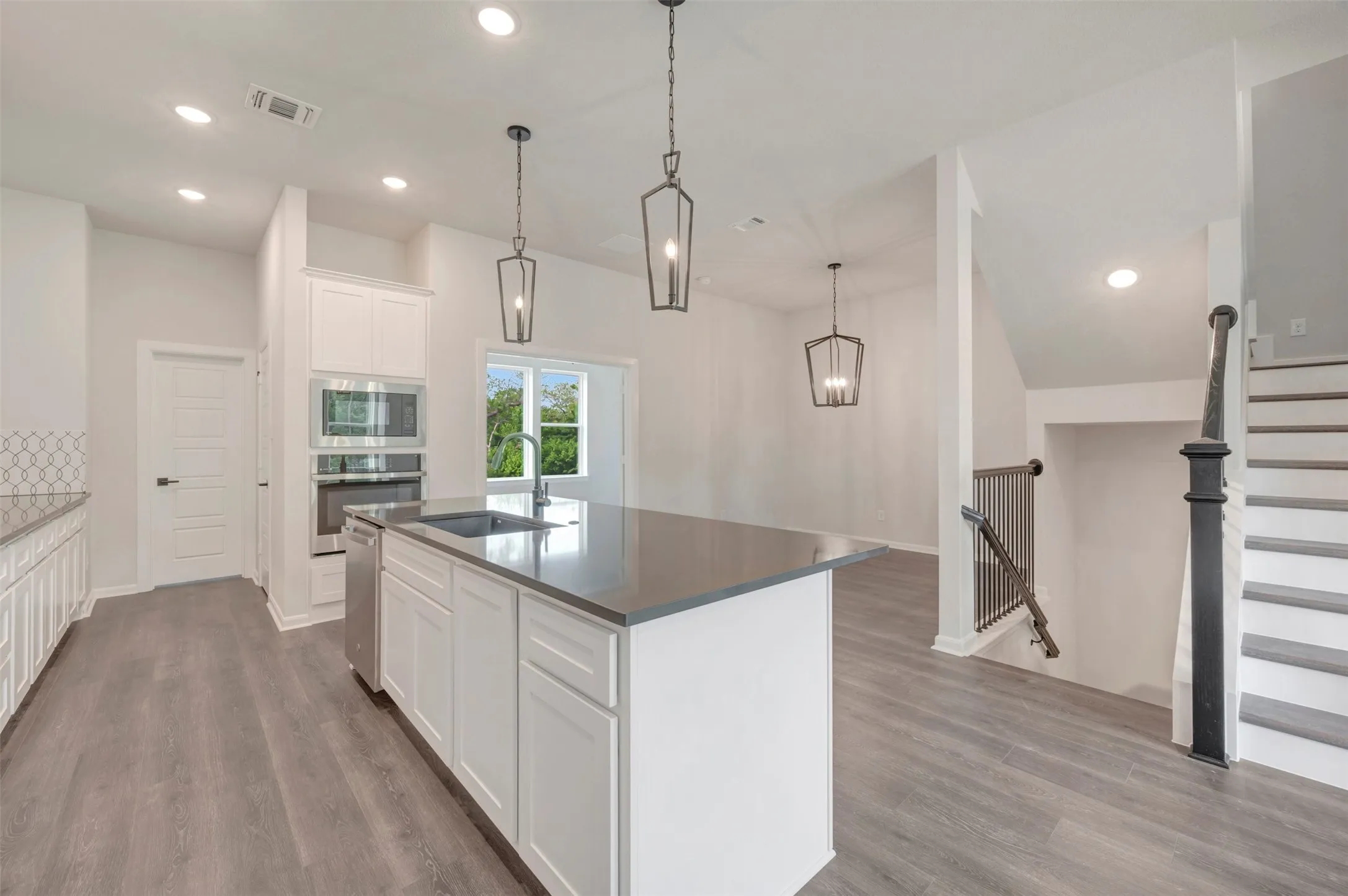 Open-concept kitchen featuring an oversized island with an undermount sink, built-in stainless steel appliances, white shaker cabinetry, and wood-finish flooring
