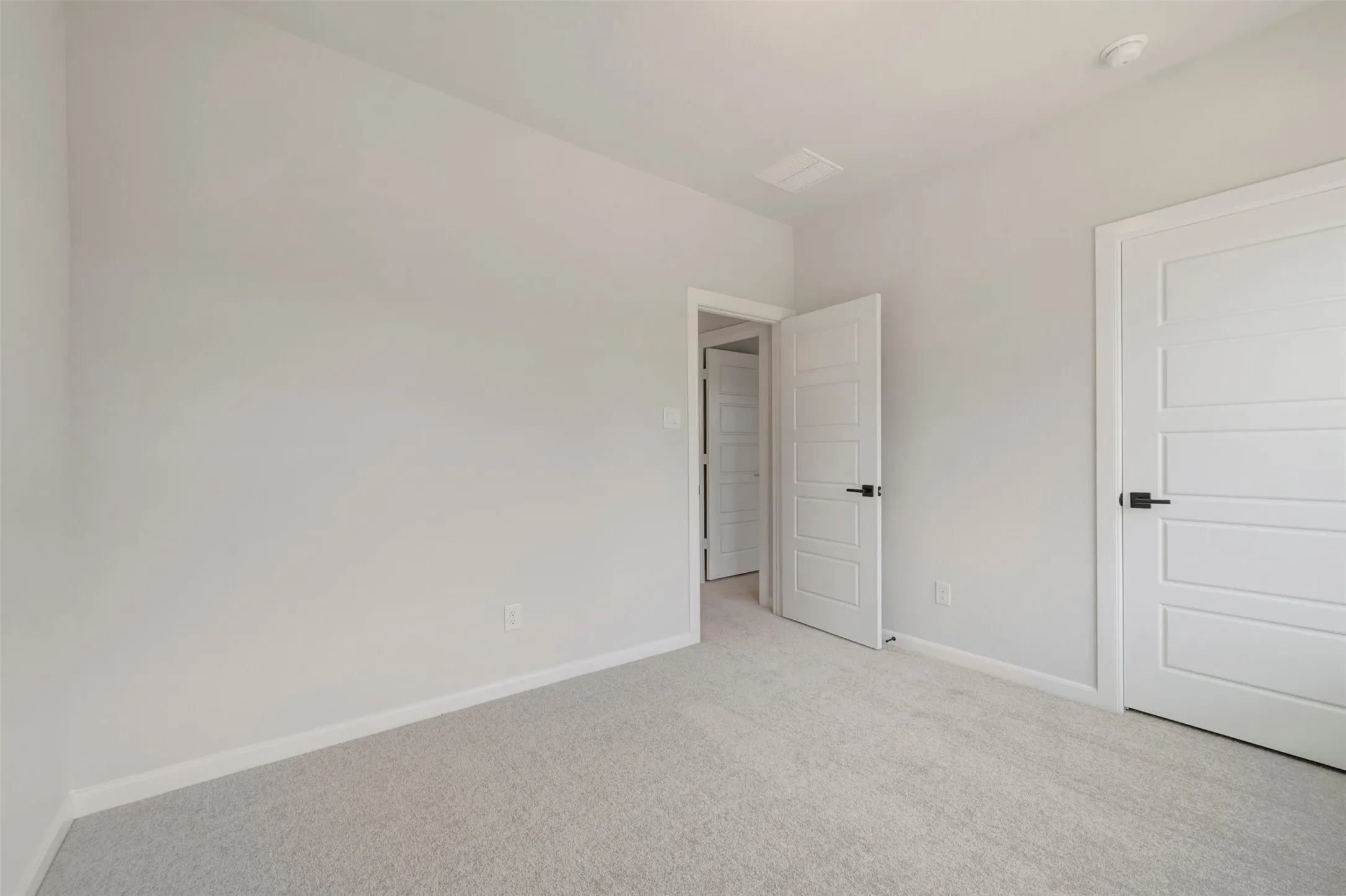 Neutral tone carpeted room with white paneled doors and matte black hardware