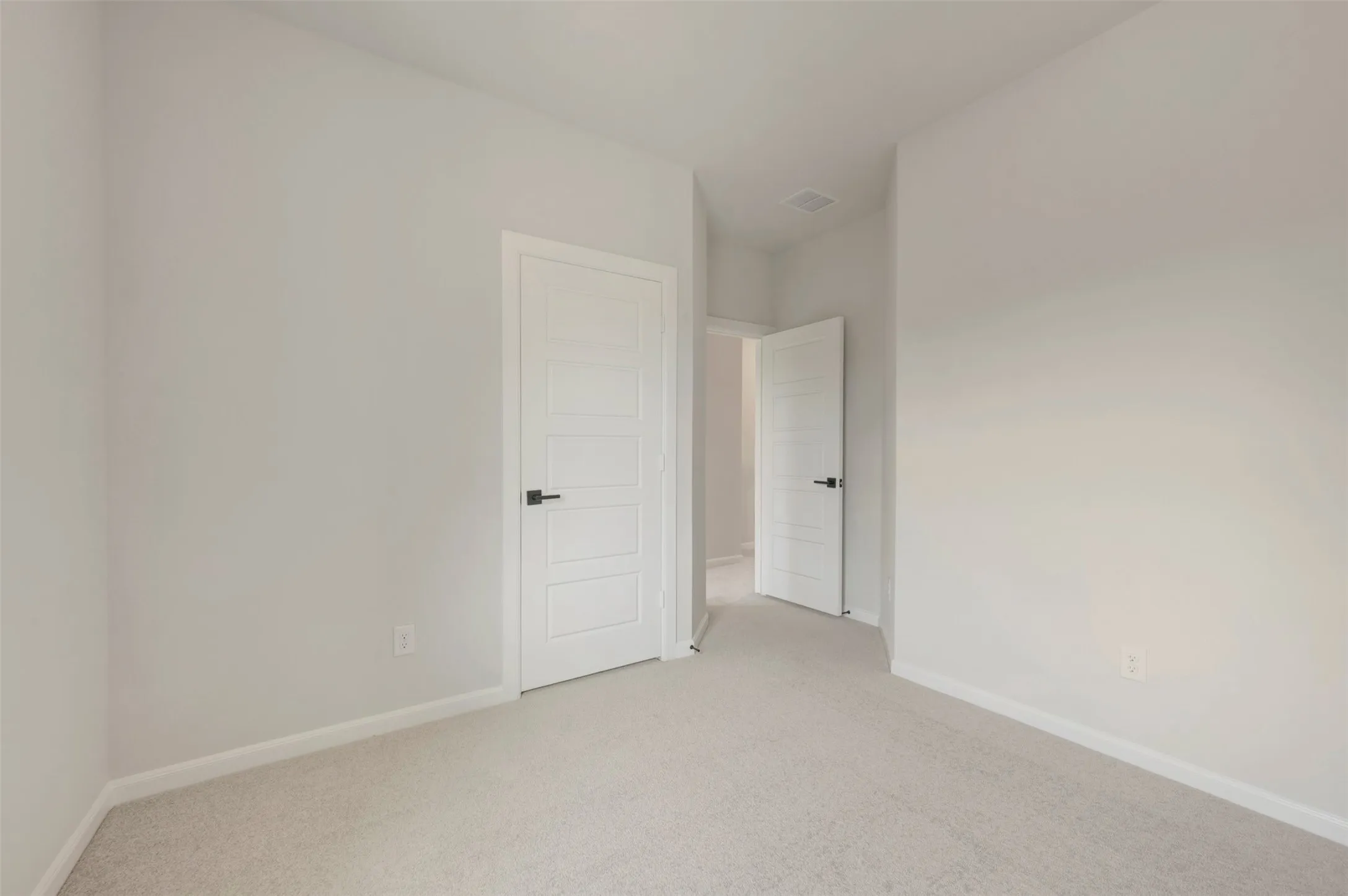 Carpeted interior space featuring light-colored walls, white trim, and white paneled doors with black hardware