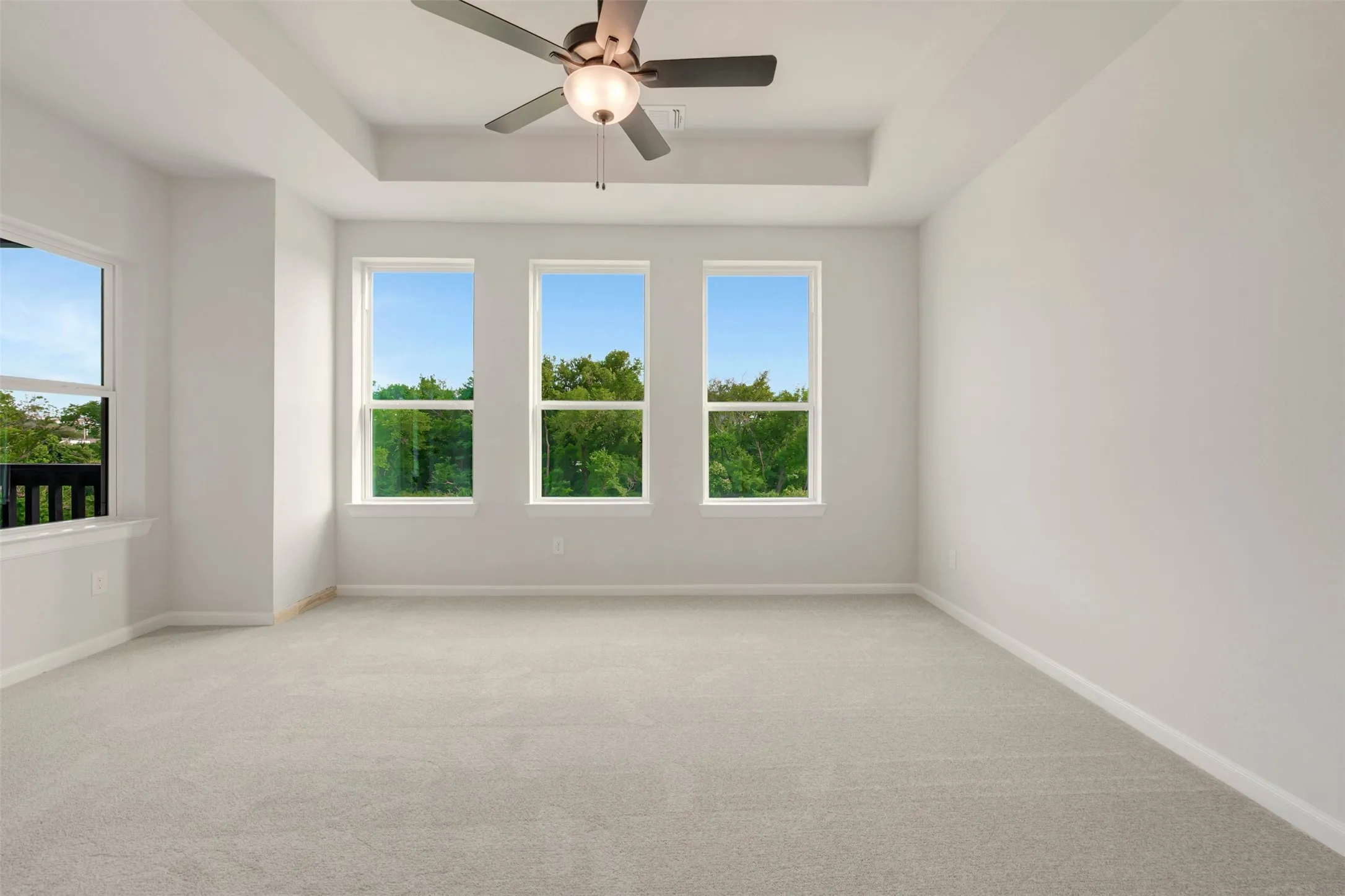Spacious room featuring light-toned carpet flooring, a tray ceiling, and a ceiling fan with integrated lighting