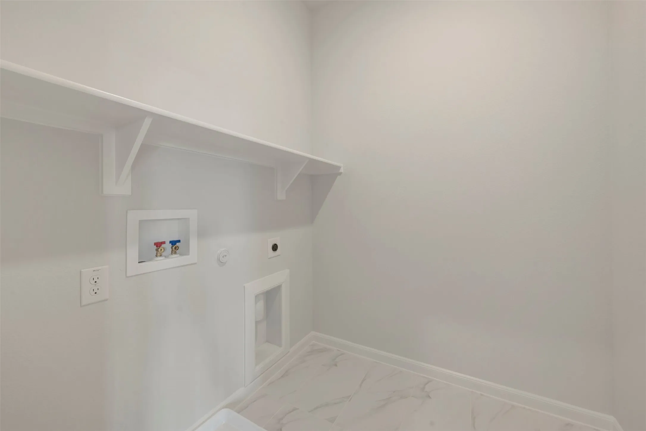 Dedicated laundry area featuring a white wall shelf, electrical outlet, washer hookups, and marble-finish flooring