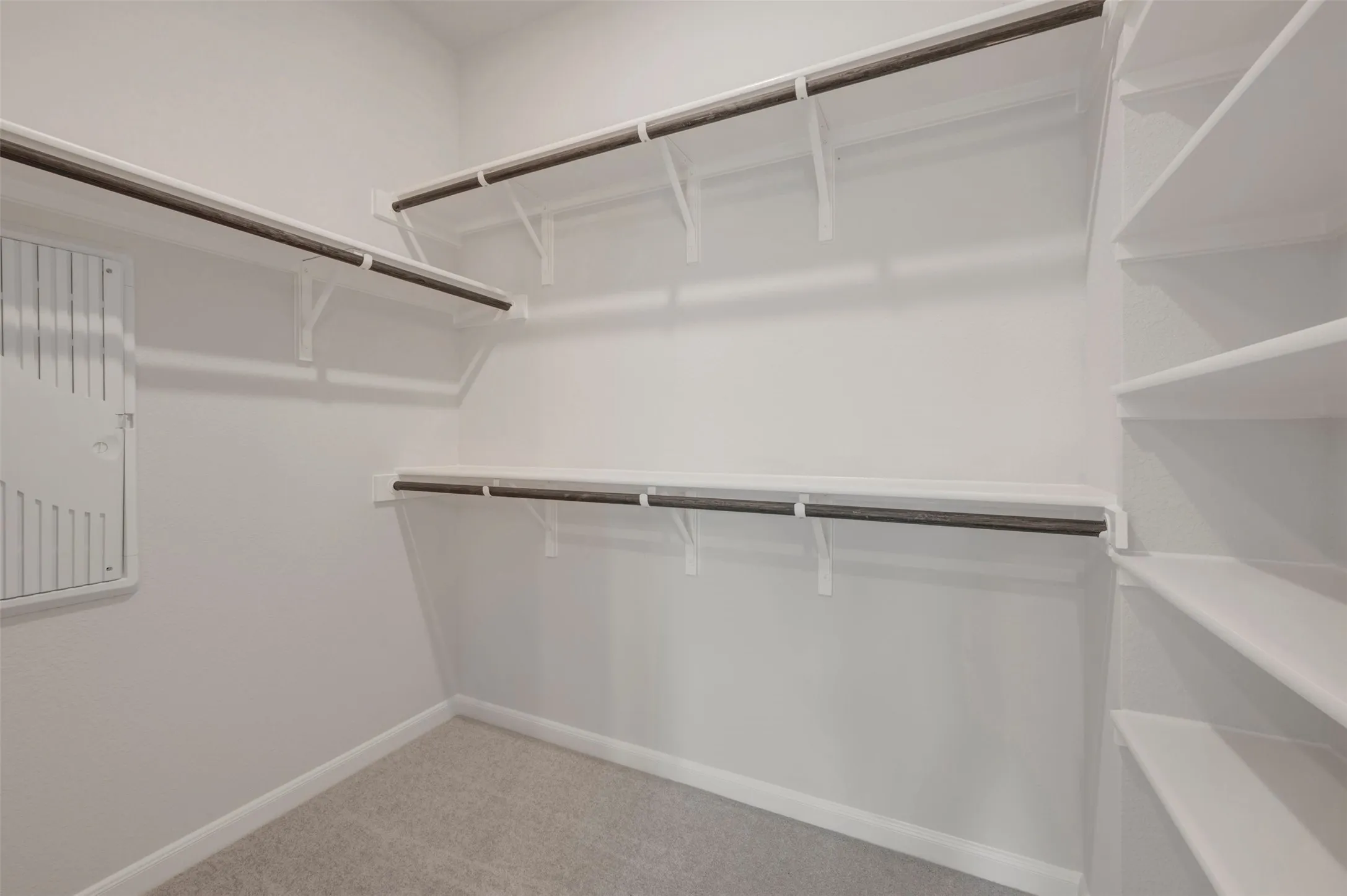 Spacious walk-in closet featuring built-in shelving, multiple hanging rods, and light-toned carpeting