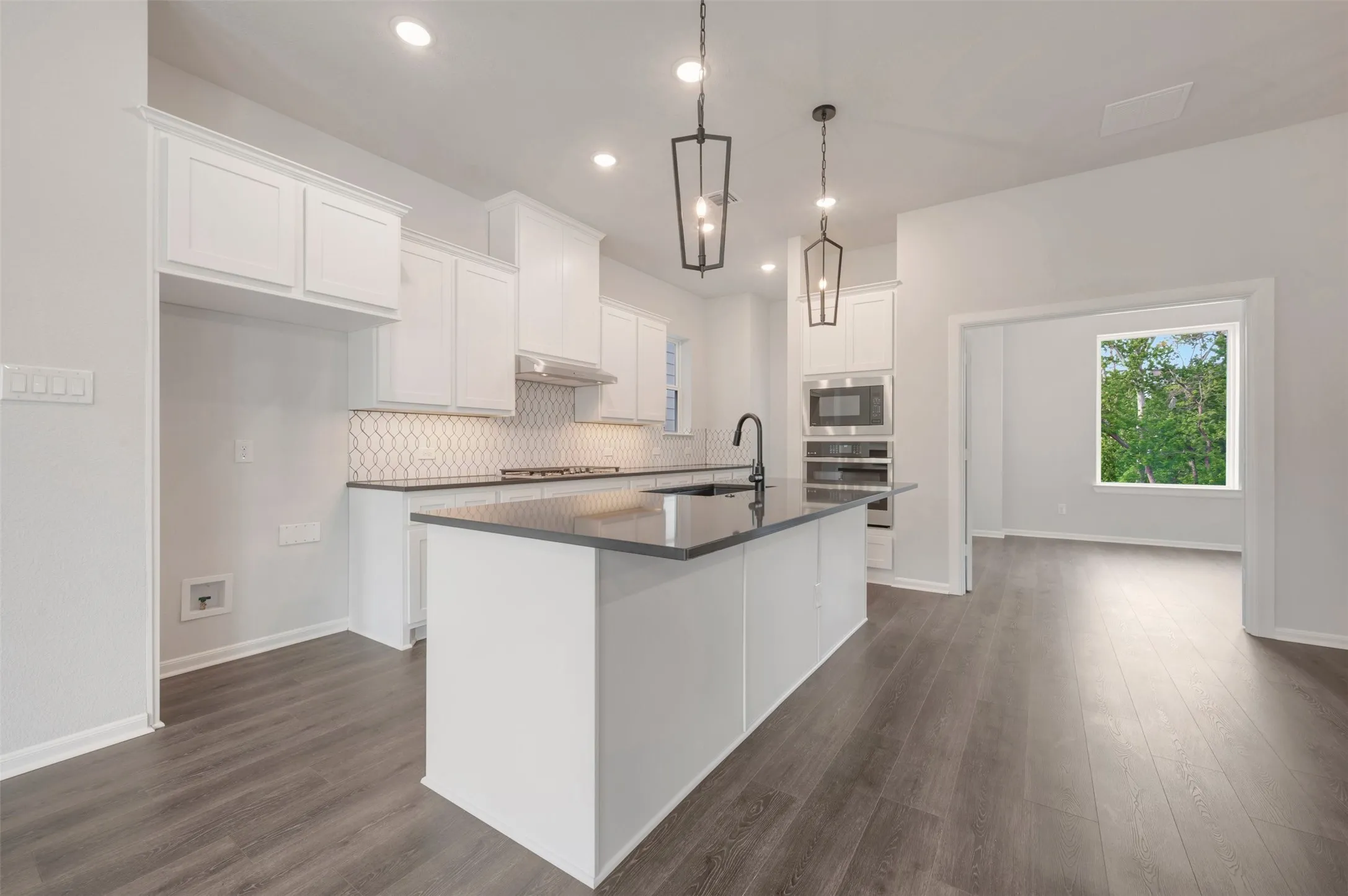Modern kitchen featuring a central island with a matte black faucet, dark countertops, and white cabinetry