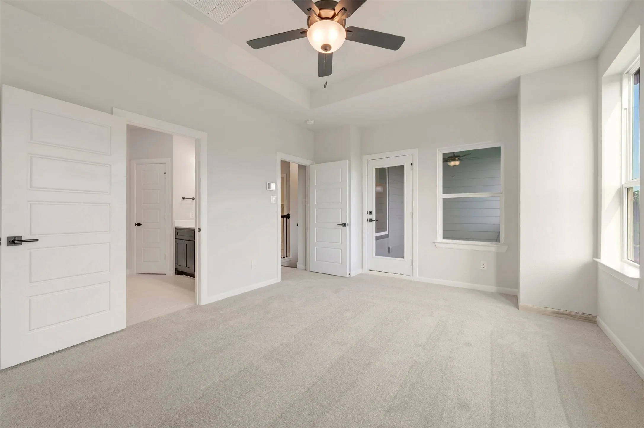 Spacious room featuring light-colored carpeting, a tray ceiling with a ceiling fan, and multiple windows