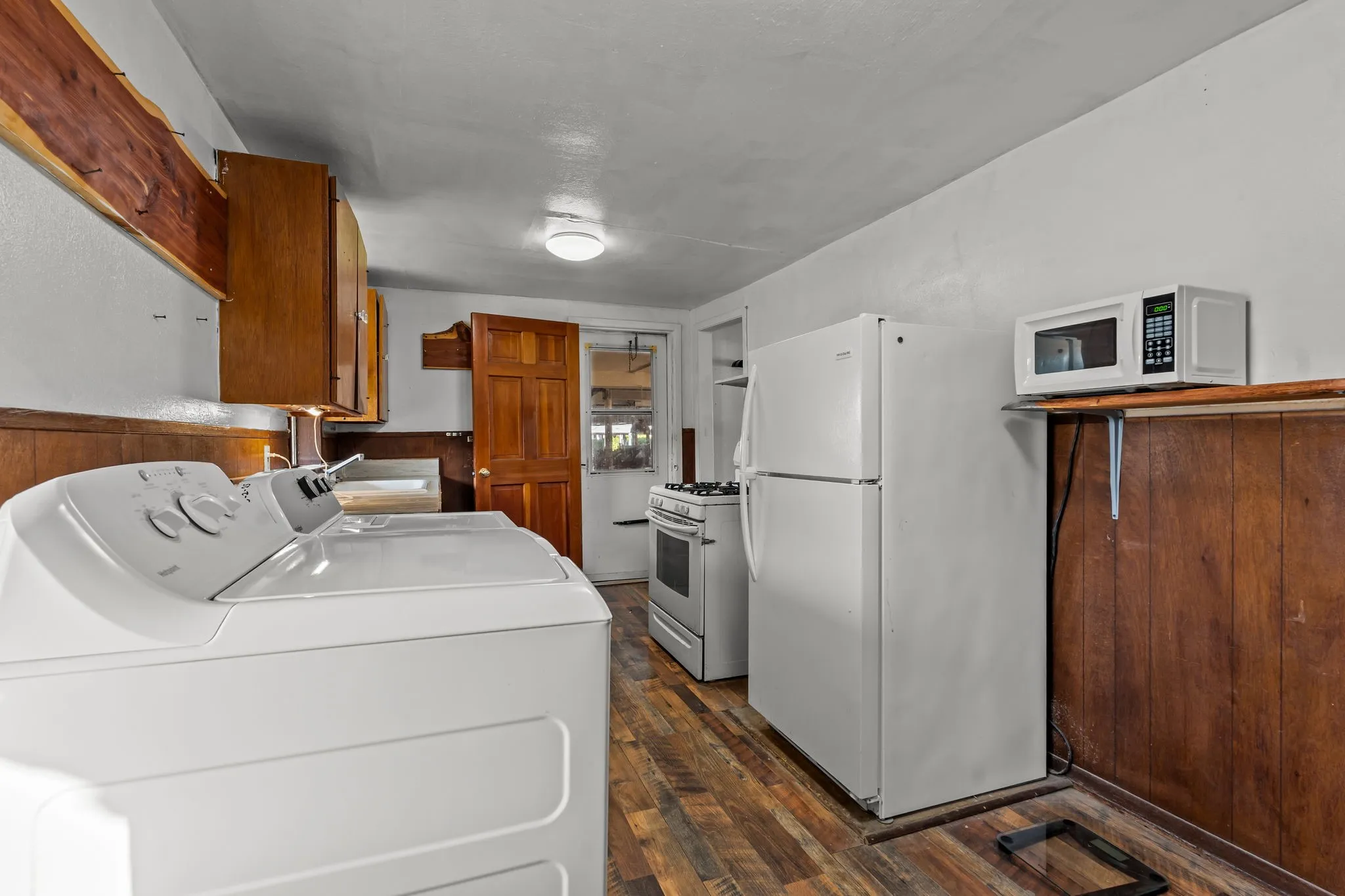 Kitchen with brown cabinets, white appliances, dark wood-style flooring, washing machine and clothes dryer, and wainscoting