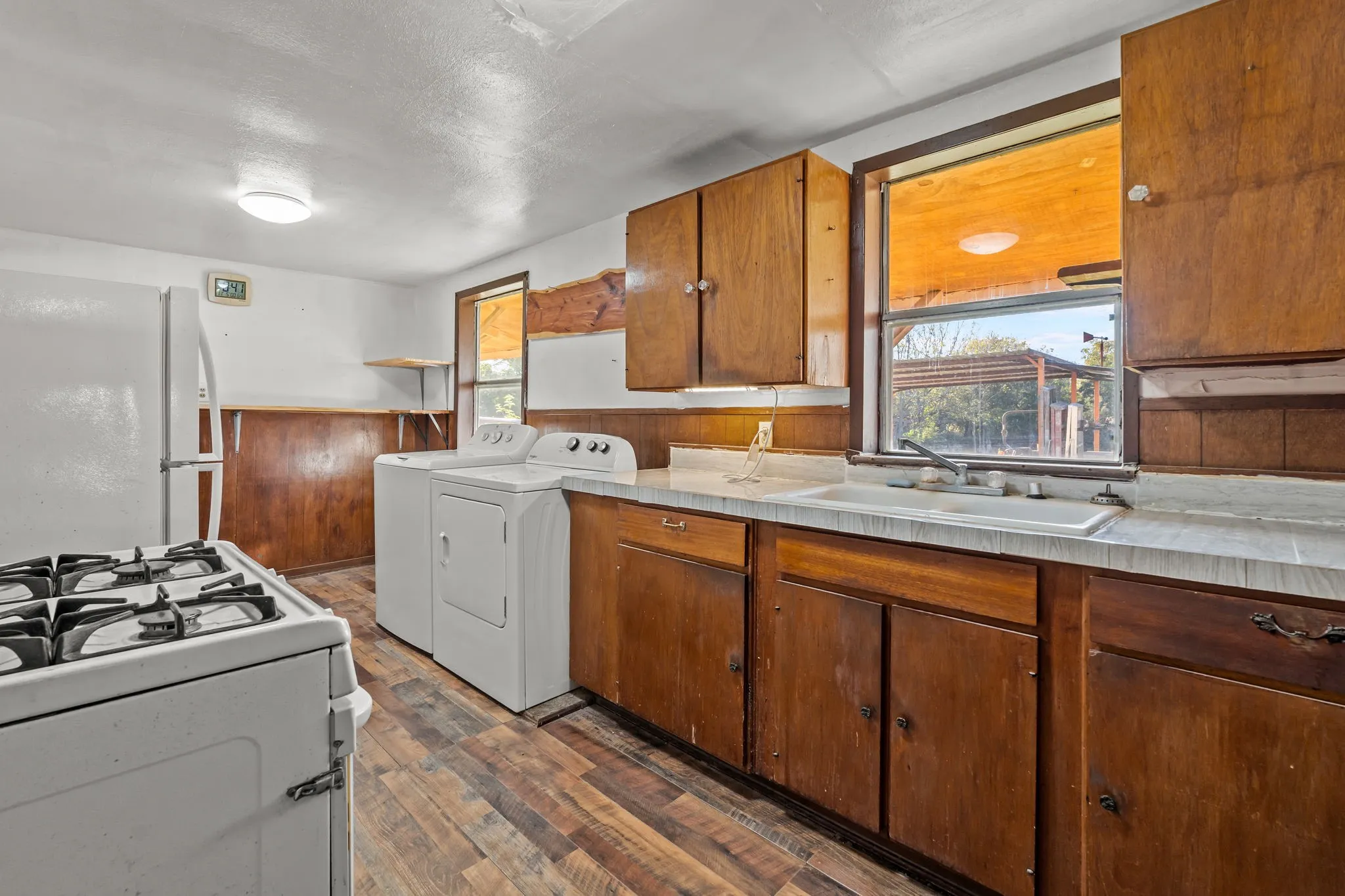 Kitchen with white appliances, light countertops, dark wood-style flooring, brown cabinetry, and washing machine and dryer