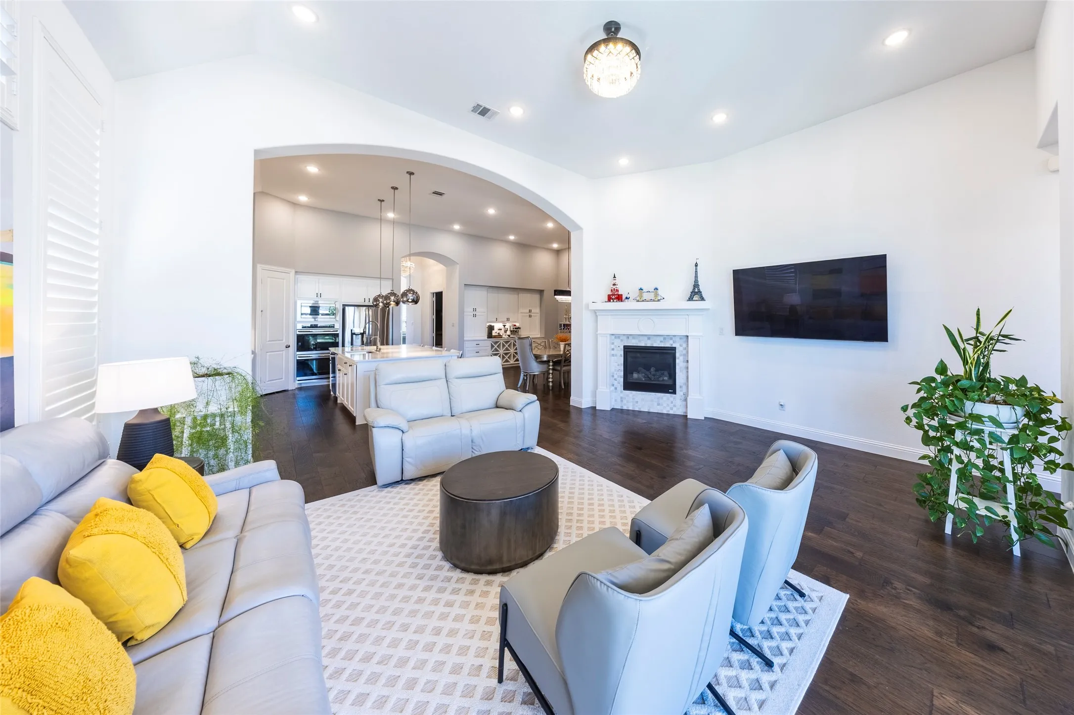 Living room with recessed lighting, dark wood-type flooring, a glass covered fireplace, arched walkways, and lofted ceiling