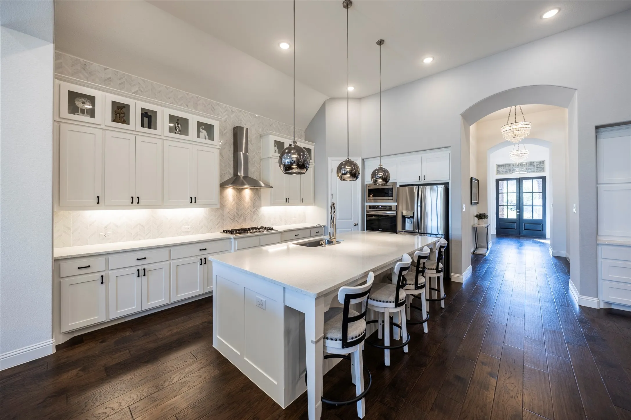 Kitchen featuring arched walkways, white cabinets, dark wood-type flooring, a breakfast bar, and high vaulted ceiling