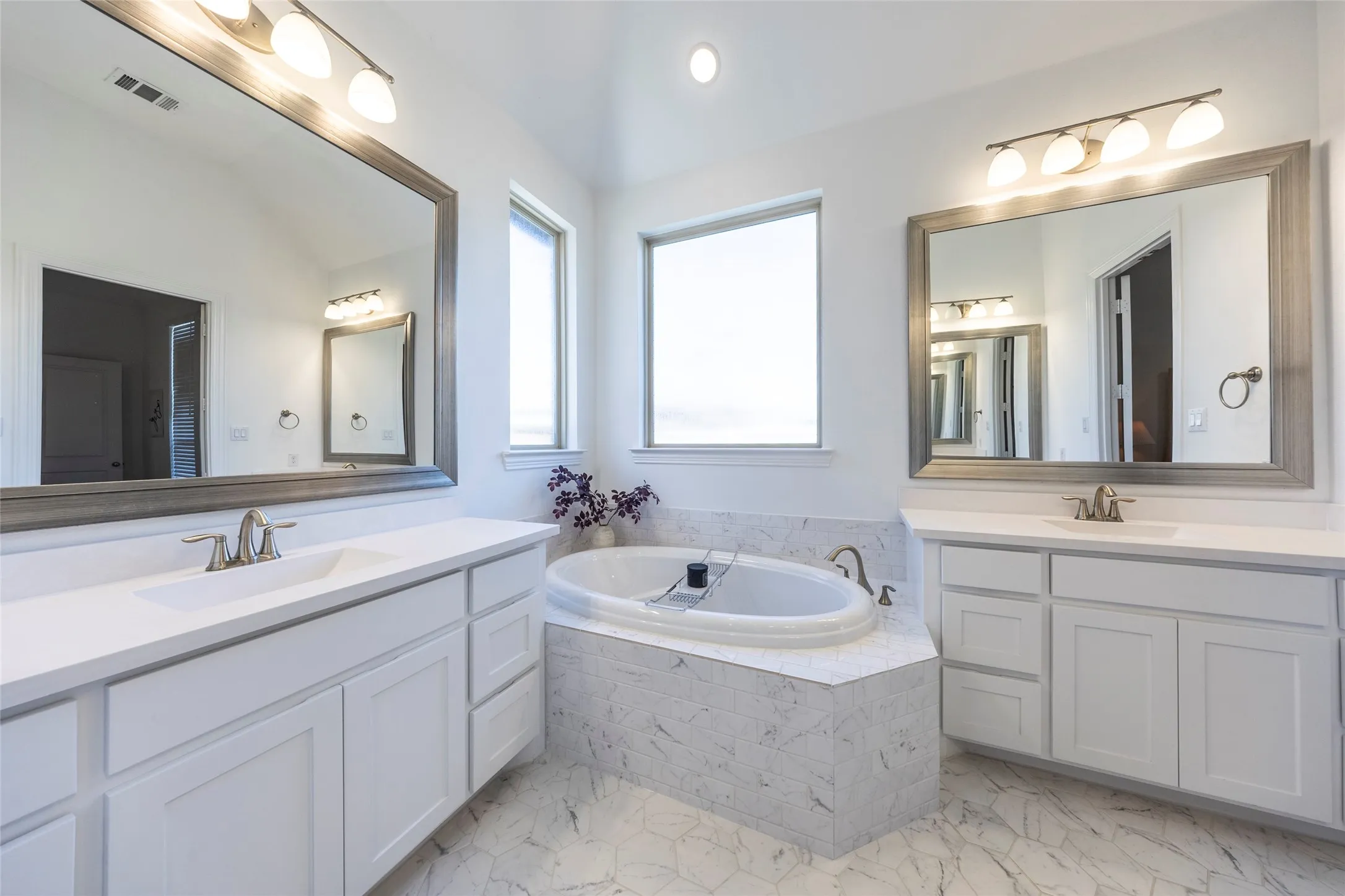 Full bath featuring two vanities, light marble finish flooring, a bath, and recessed lighting