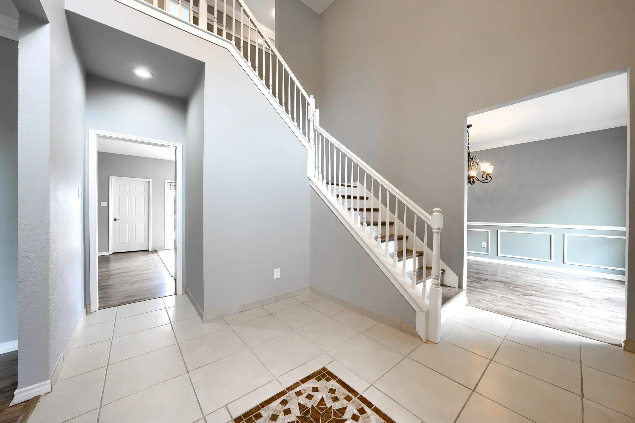 Grand foyer featuring a white baluster staircase and light-toned tile flooring with a decorative mosaic inlay