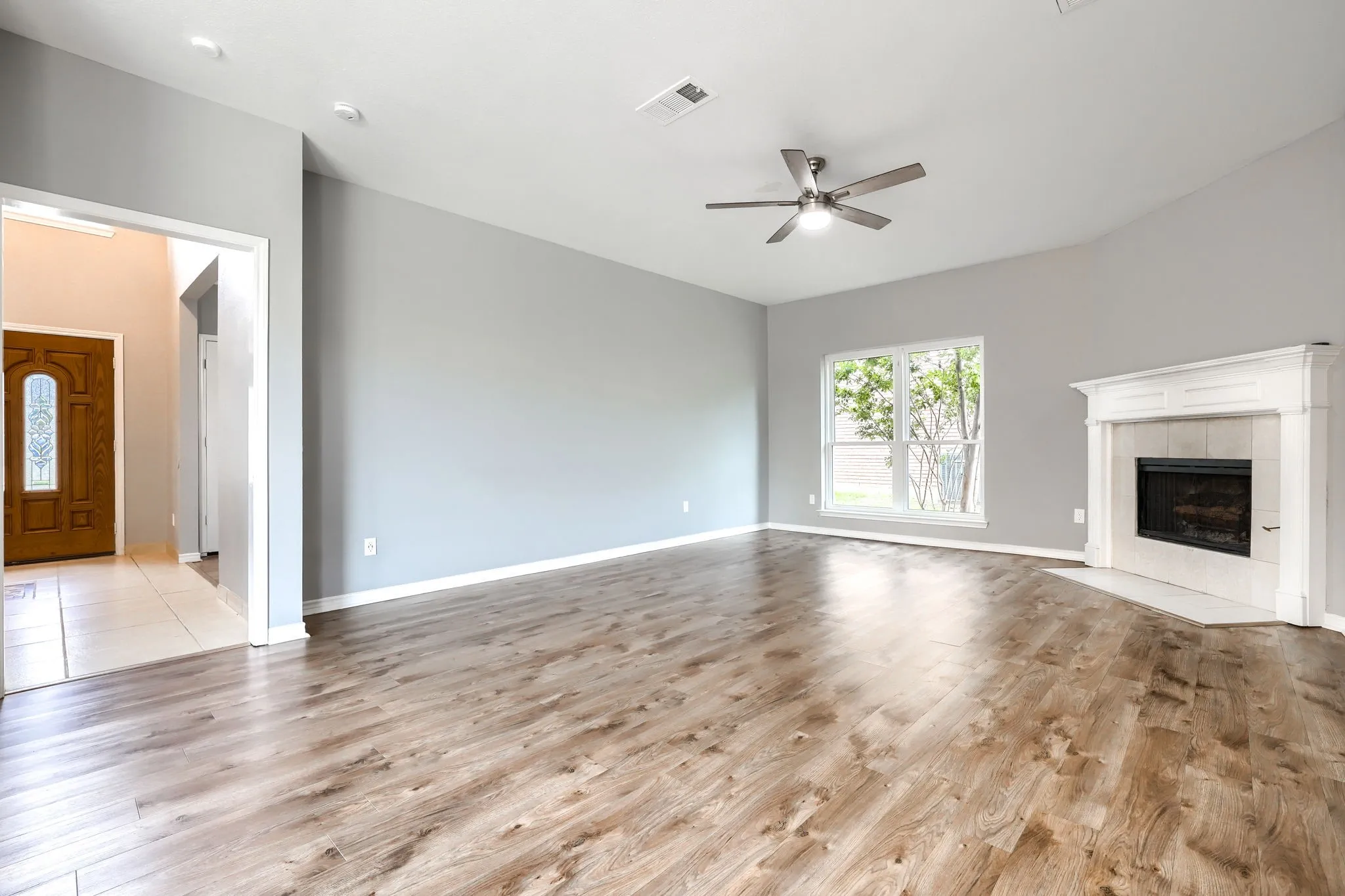 Spacious living area featuring high vaulted ceilings, wood-finish flooring, a white mantel fireplace with tile surround, and a ceiling fan with integrated lighting