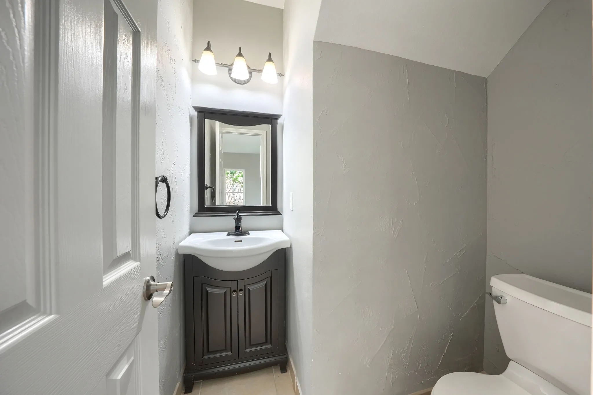 Powder room featuring a dark wood-finish vanity with an integrated white sink, a framed mirror, and a three-light vanity fixture