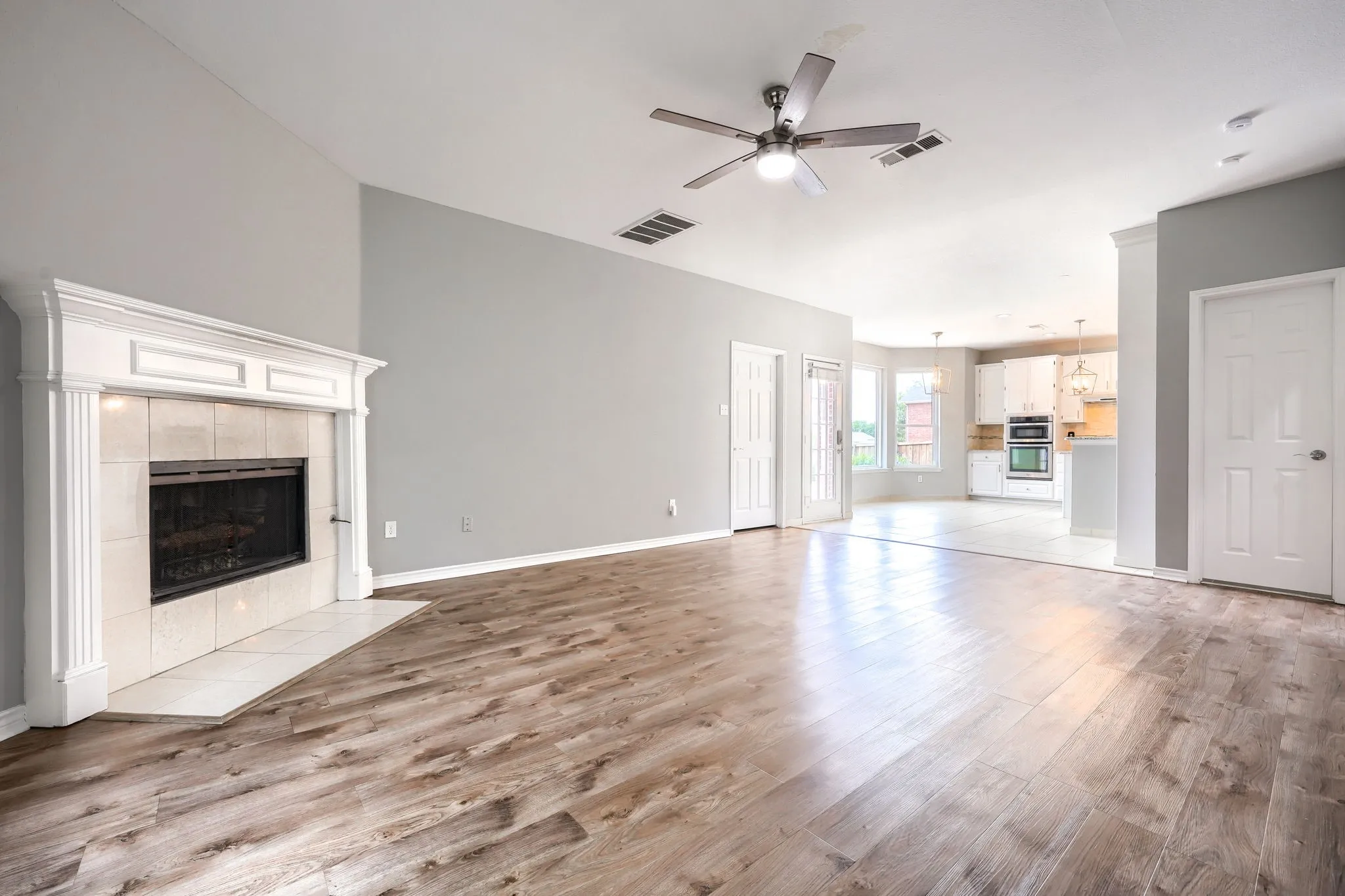Spacious living area featuring wood-finish flooring, a white mantel fireplace with tile surround, and vaulted ceilings with a ceiling fan