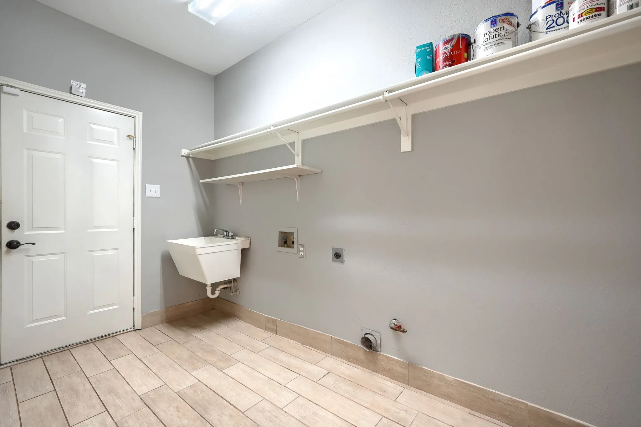 Utility room featuring wood-finish tile flooring, a wall-mounted utility sink, and built-in shelving
