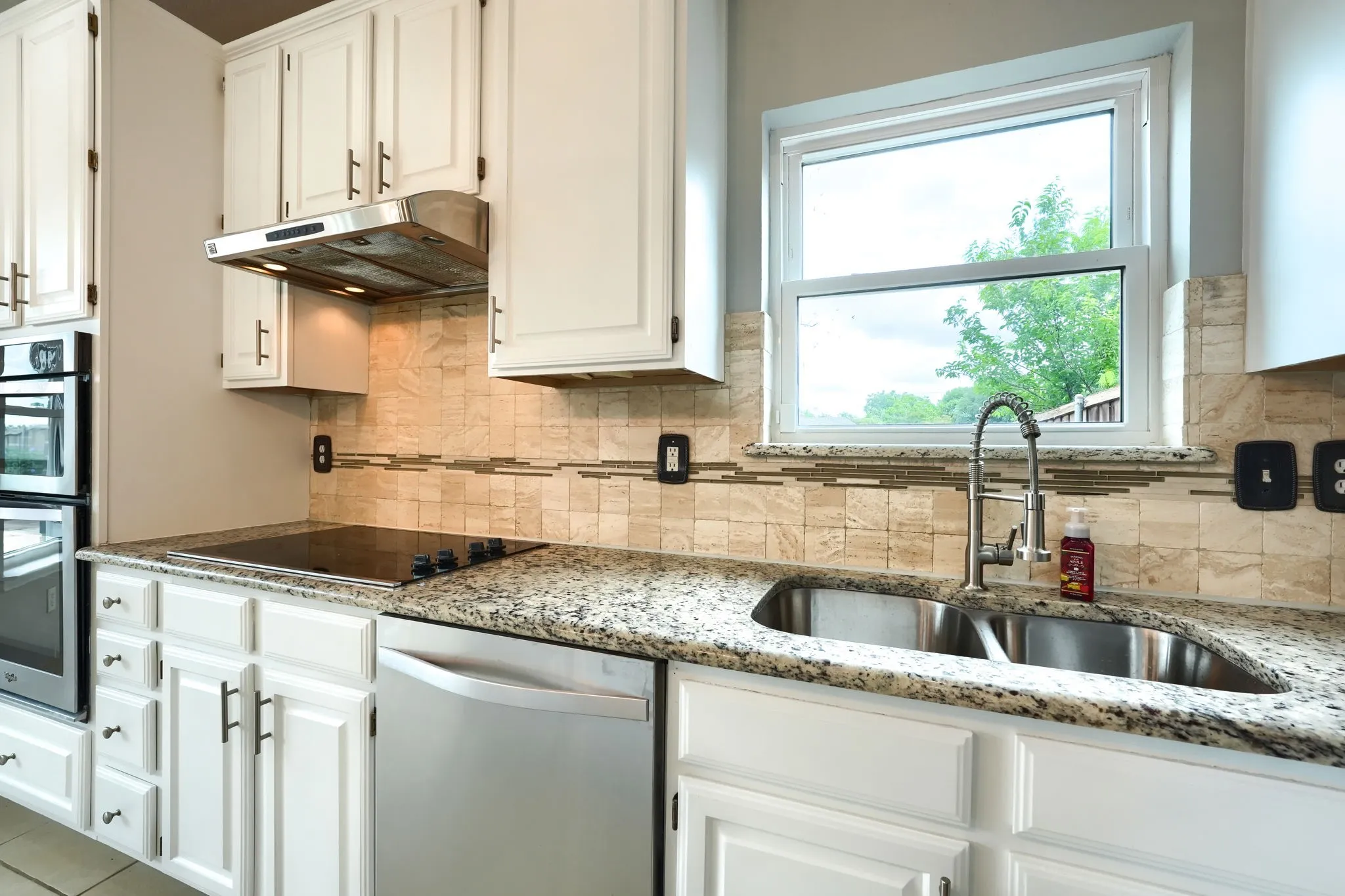 Kitchen featuring white cabinetry, granite countertops, a stainless steel double sink with a gooseneck faucet, an electric cooktop, and a mosaic tile backsplash