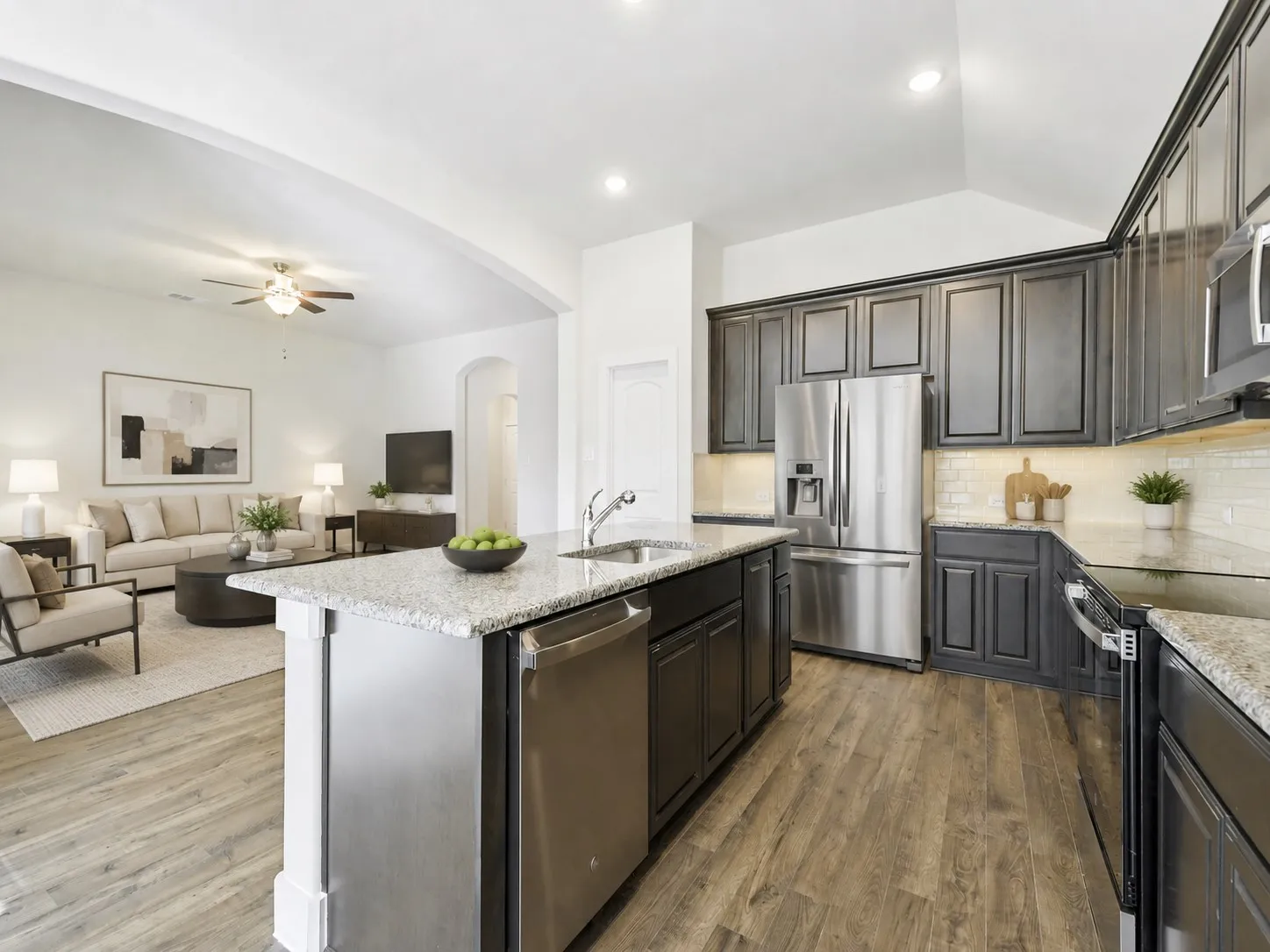 Kitchen featuring a central island with an integrated sink and dishwasher, wood-finish flooring, dark cabinetry, and light-toned countertops