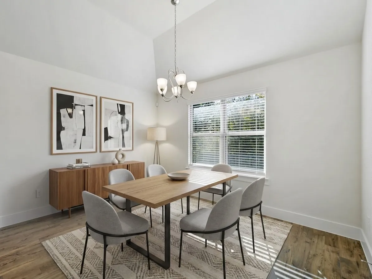 Vaulted ceiling dining area featuring wood-finish flooring, a contemporary chandelier, and a large window with blinds