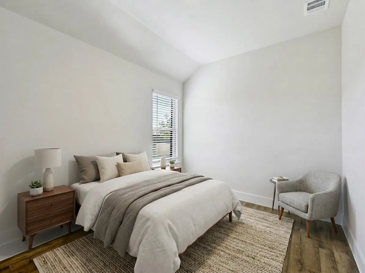 White walls and wood-finish flooring define this bright room with a single window featuring horizontal blinds