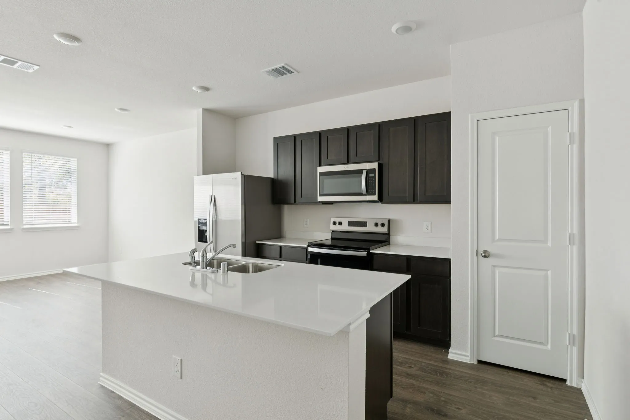 Kitchen with appliances with stainless steel finishes, dark wood-type flooring, a center island with sink, light stone countertops, and dark cabinetry