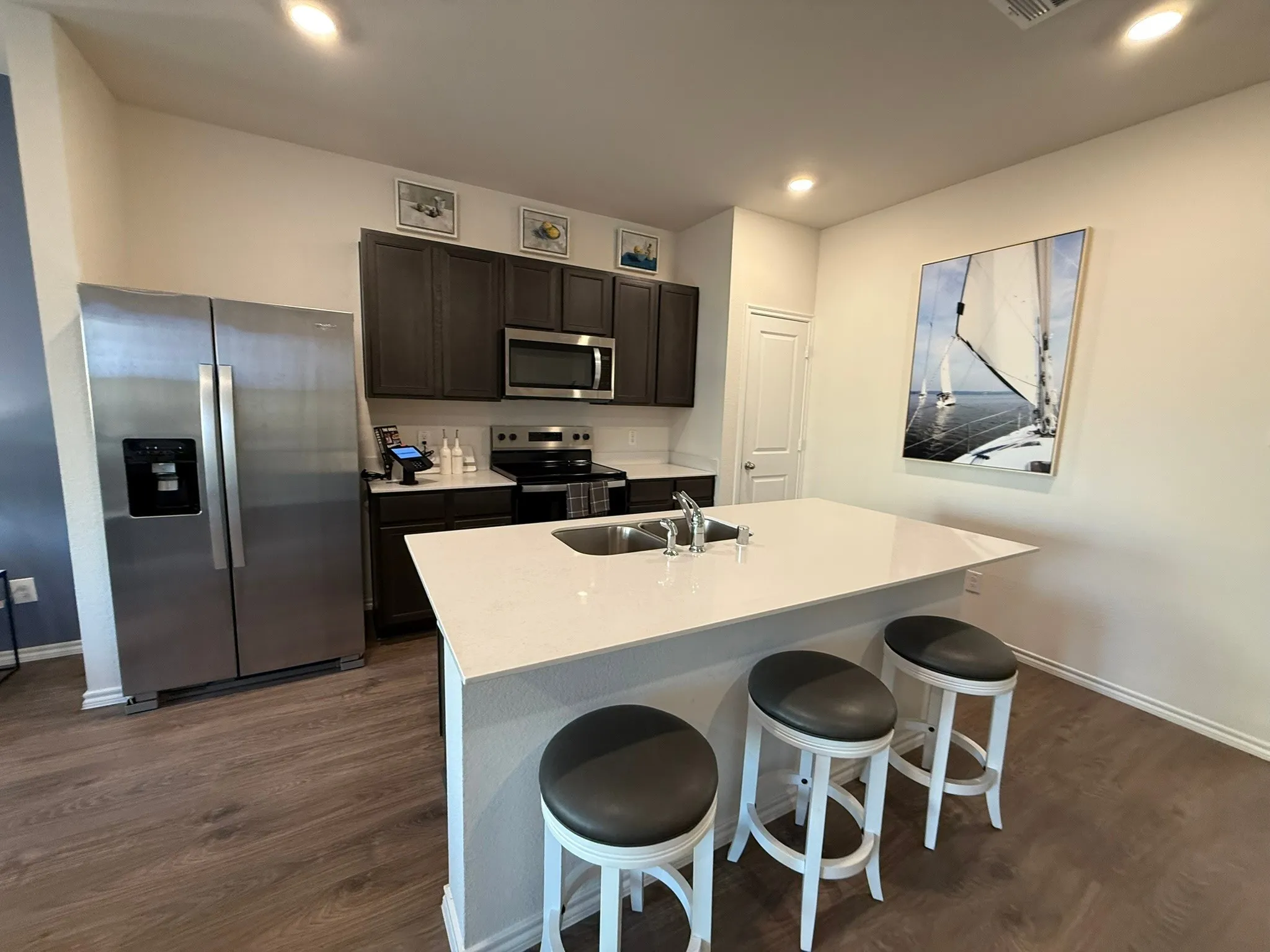 Kitchen with appliances with stainless steel finishes, dark wood-style floors, a kitchen island with sink, a breakfast bar area, and light stone counters
