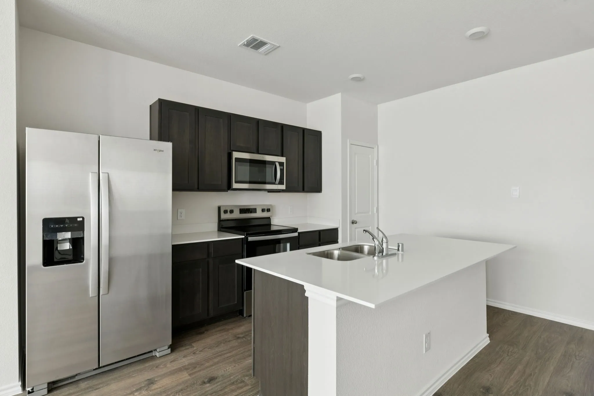 Kitchen featuring stainless steel appliances, a center island with sink, dark wood-style floors, and light stone countertops