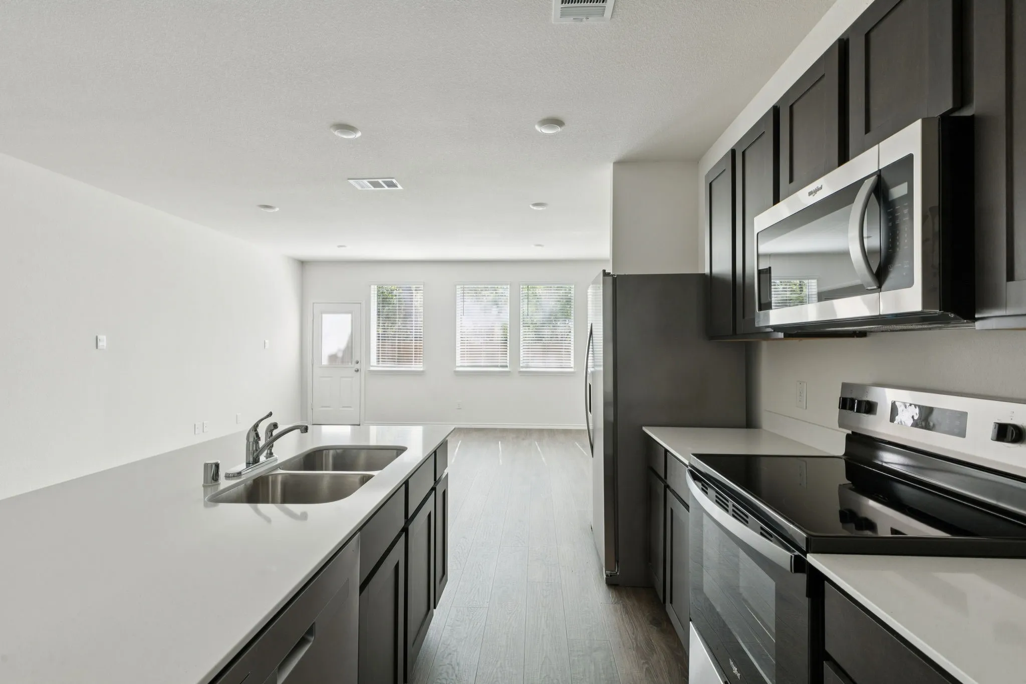 Kitchen featuring appliances with stainless steel finishes, dark cabinetry, wood finished floors, and light stone countertops