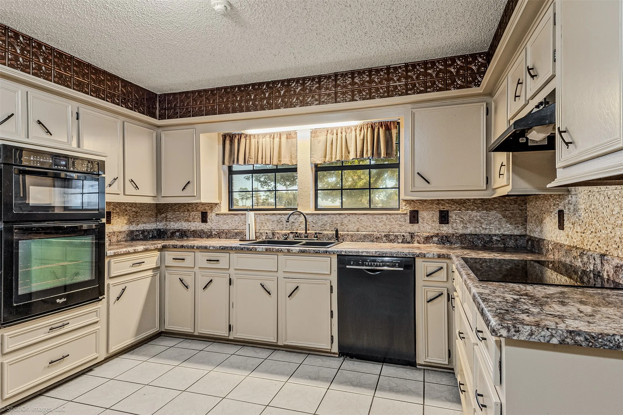Kitchen featuring black appliances, light tile patterned floors, a textured ceiling, backsplash, and cream cabinetry