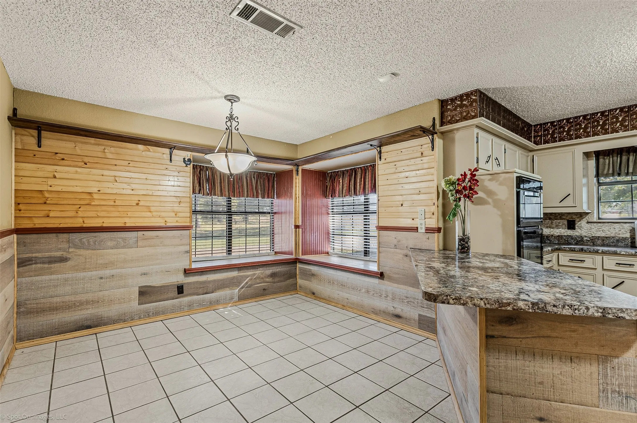 Unfurnished dining area with light tile patterned floors, wooden walls, a textured ceiling, and a wainscoted wall