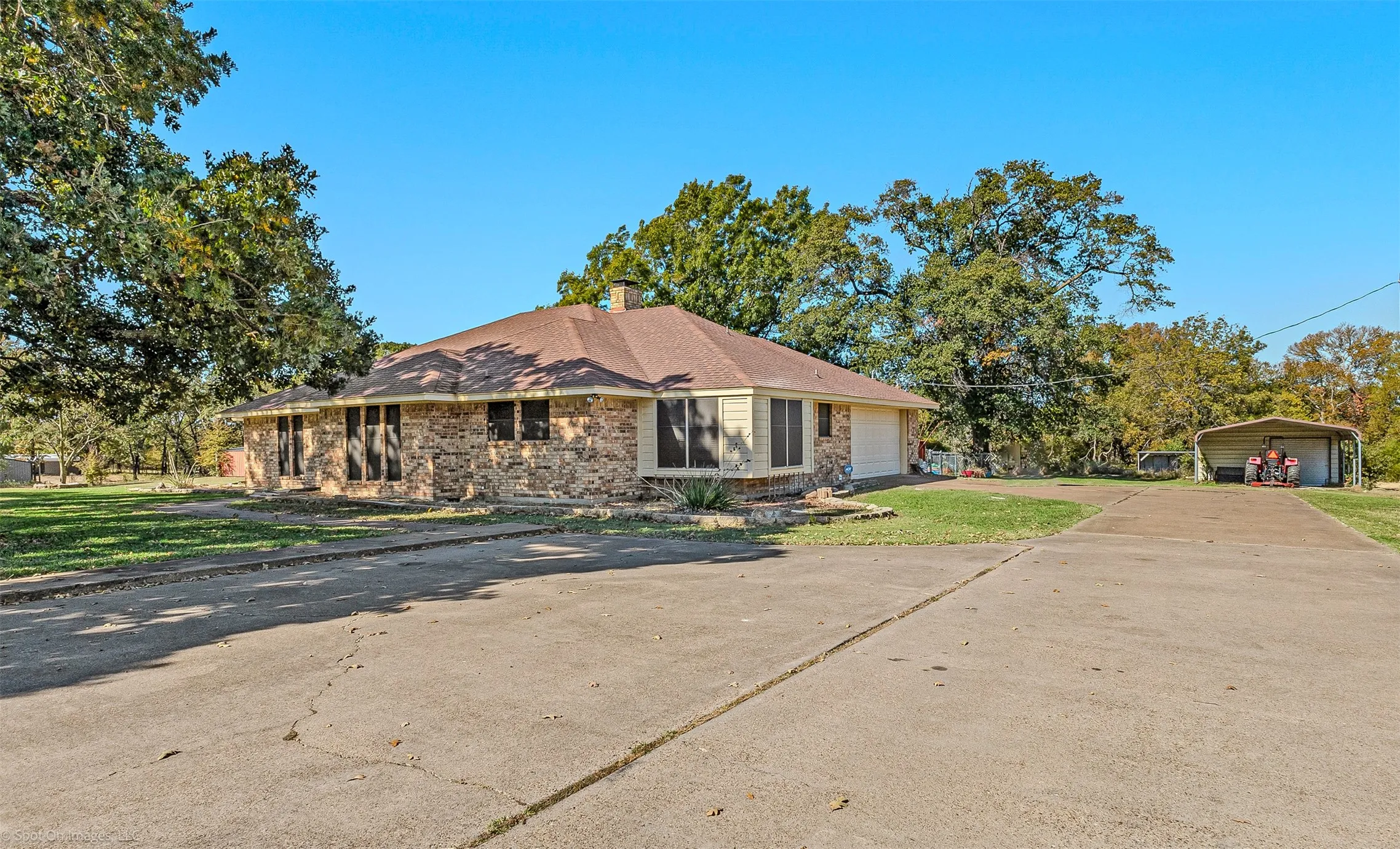View of front of property featuring a detached carport, concrete driveway, a front lawn, and a chimney