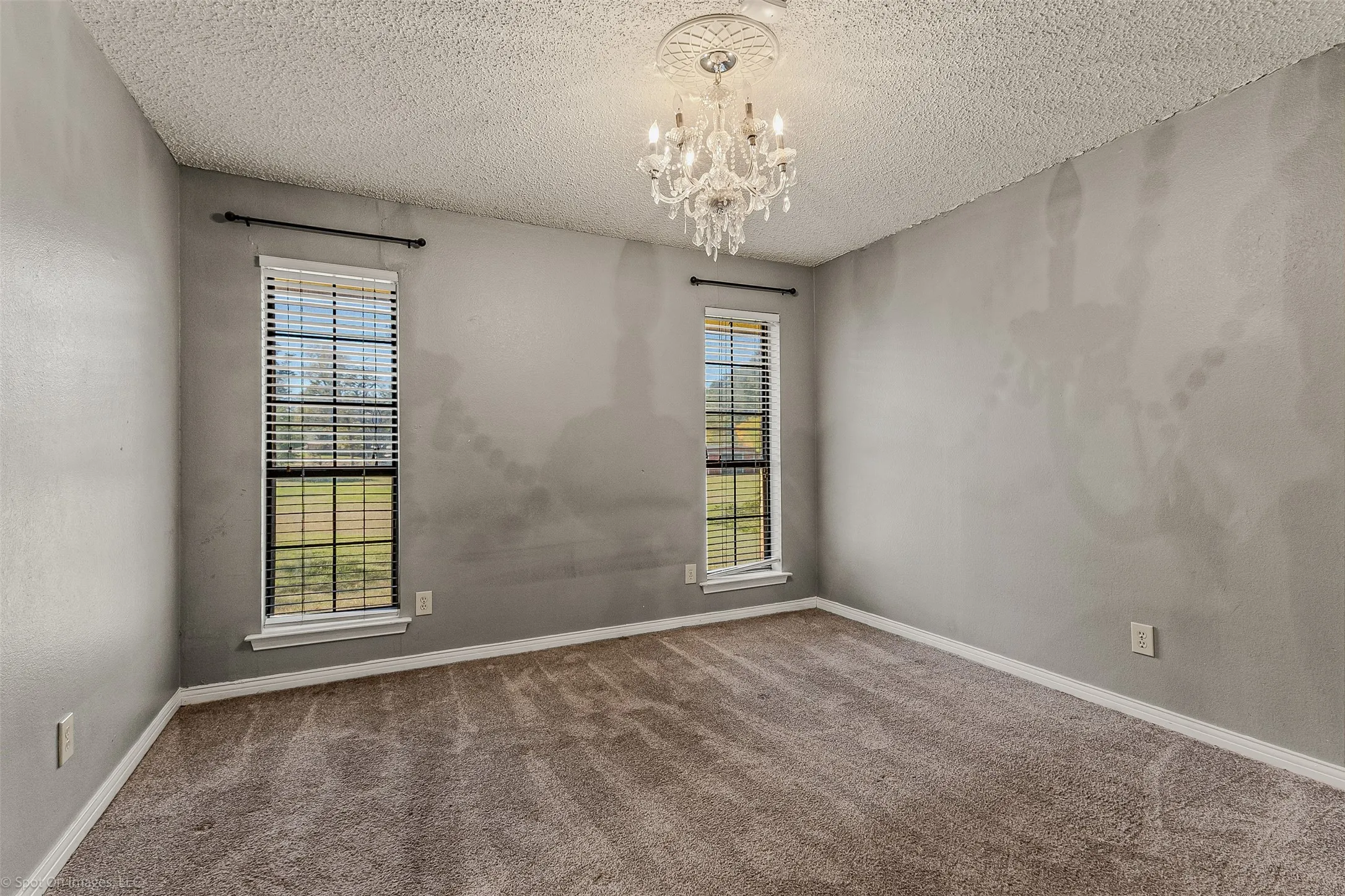 Carpeted empty room with a textured ceiling, a chandelier, and a textured wall