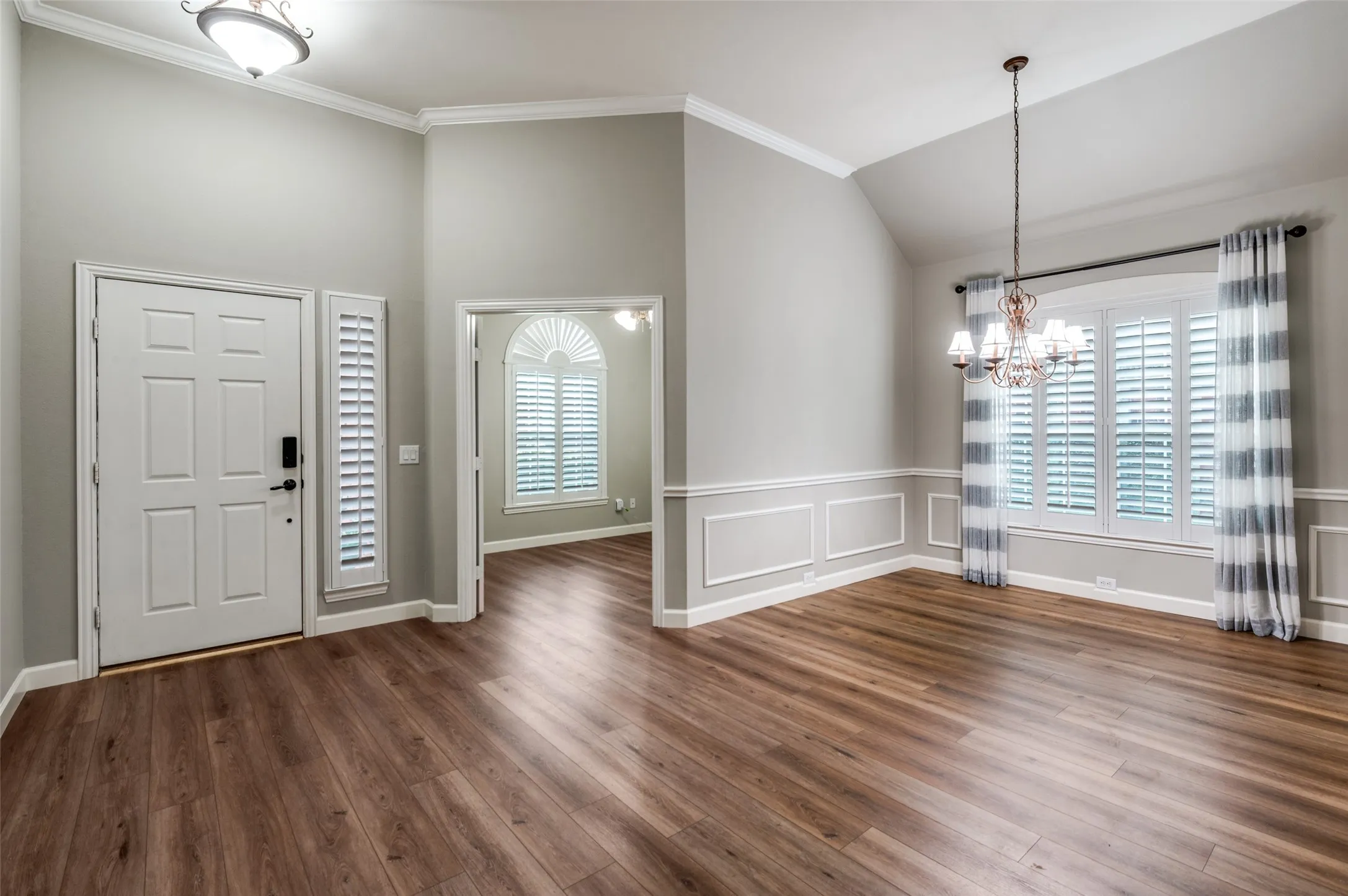 Foyer entrance with a chandelier, dark wood-style floors, plenty of natural light, lofted ceiling, and crown molding