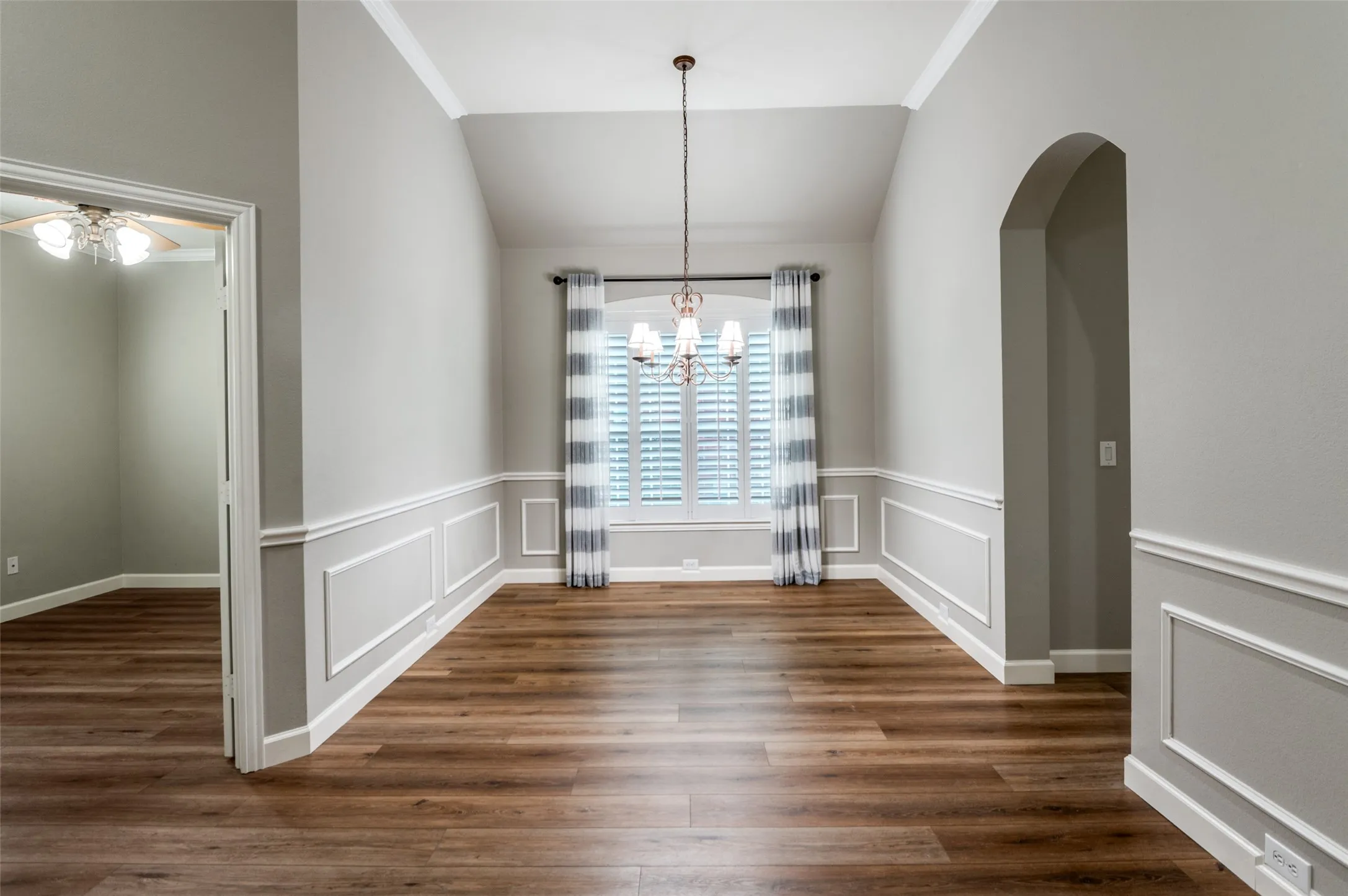 Unfurnished dining area featuring dark wood-style floors, a chandelier, vaulted ceiling, crown molding, and arched walkways