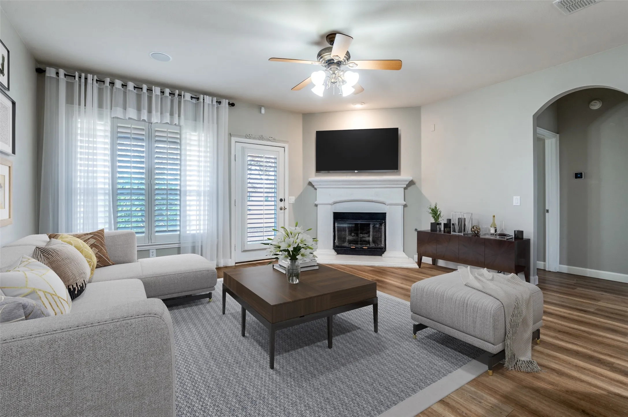 Virtual Staged Family room featuring arched walkways, a glass covered fireplace, wood finished floors, and a ceiling fan