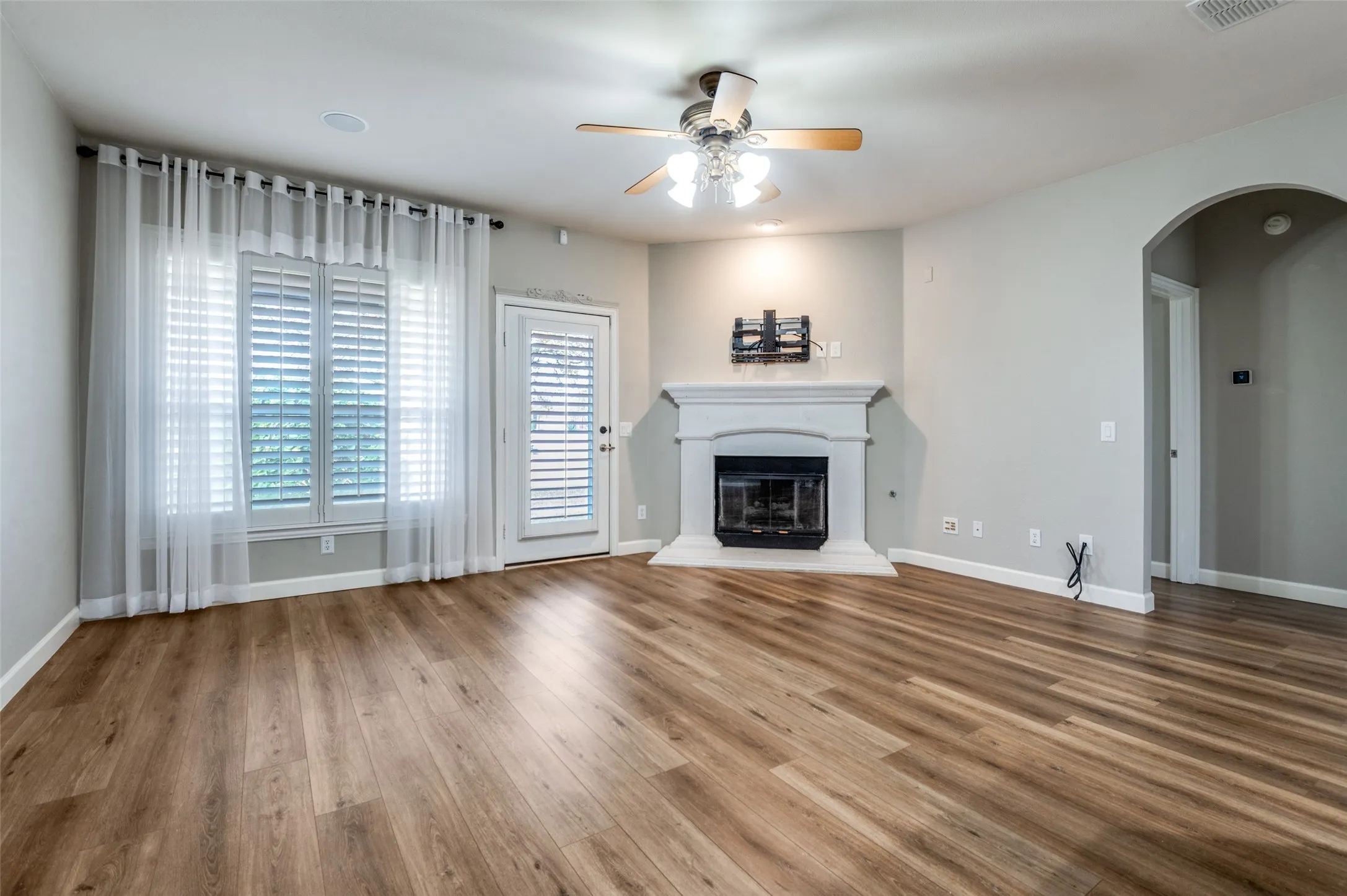 Unfurnished living room with arched walkways, a glass covered fireplace, ceiling fan, and wood finished floors