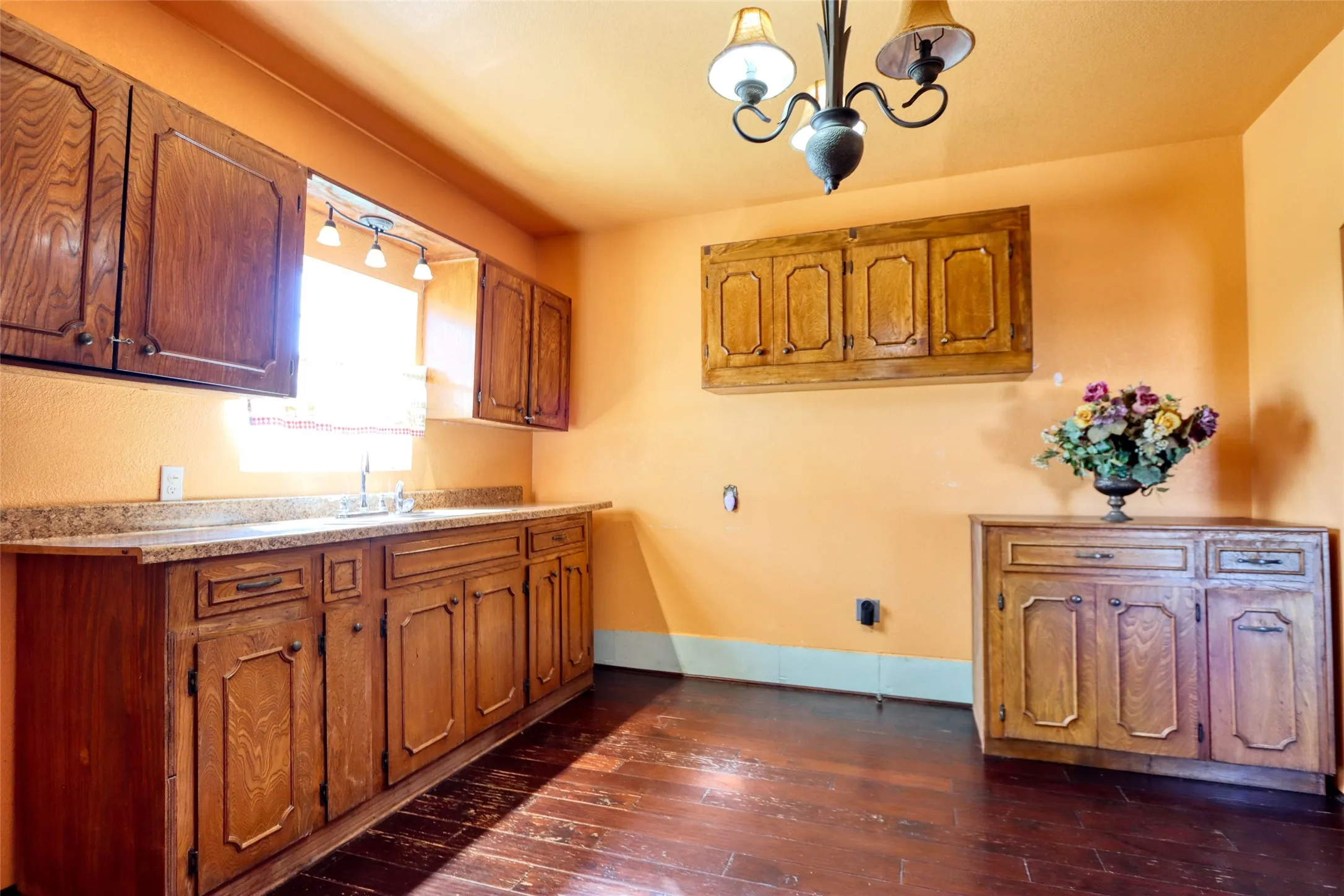 Kitchen with brown cabinetry, dark wood-style floors, light countertops, decorative light fixtures, and a chandelier