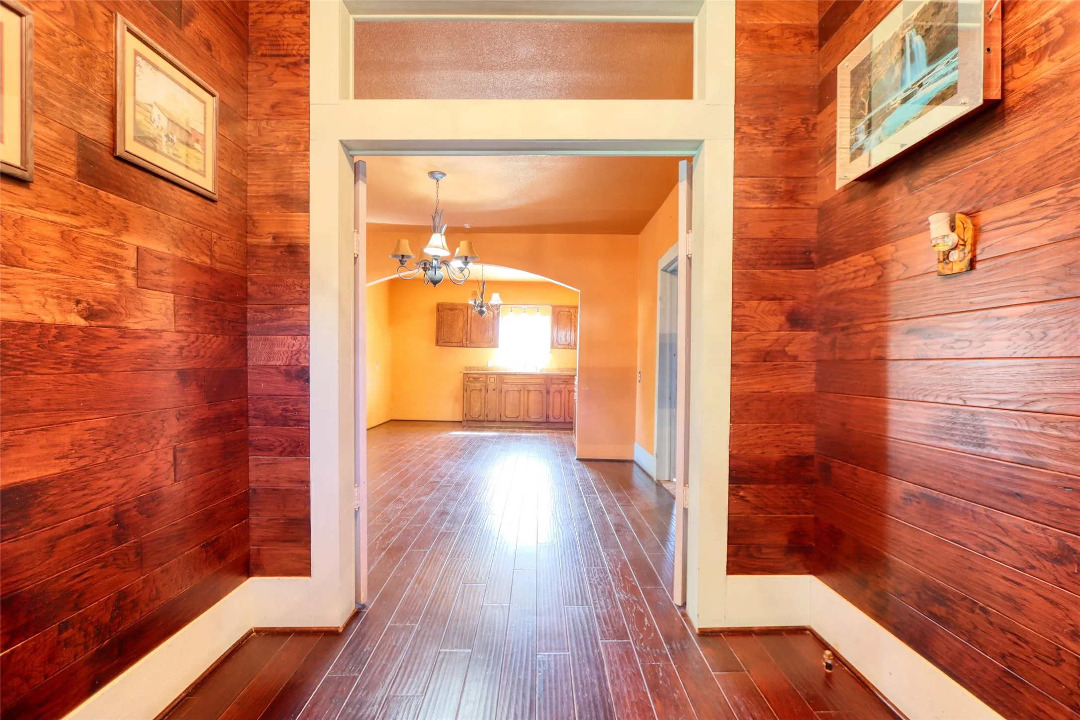 Hallway with a chandelier, wooden walls, dark wood finished floors, and arched walkways