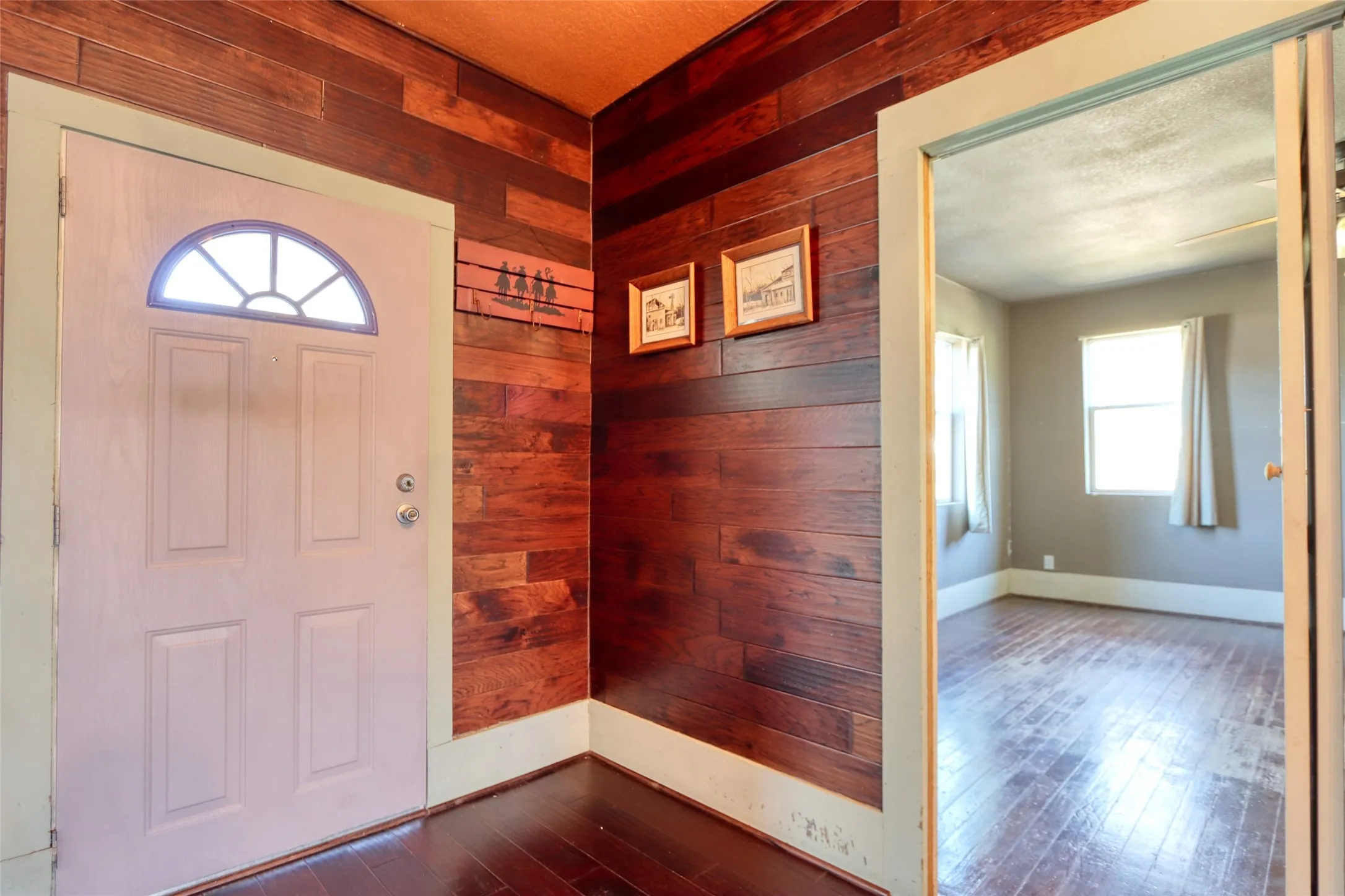 Foyer entrance with healthy amount of natural light, dark wood finished floors, wood walls, and a textured ceiling