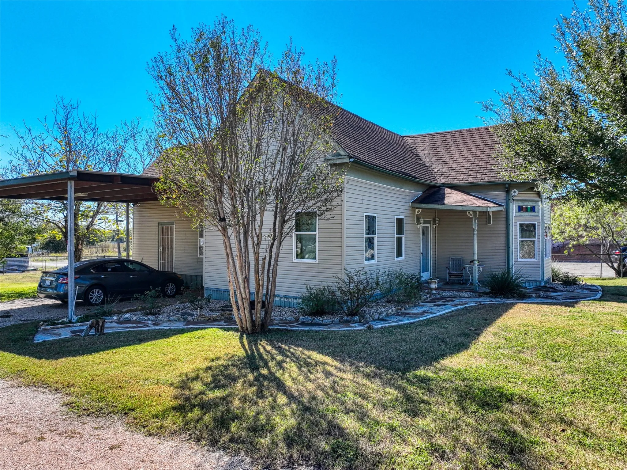 View of front facade with a front yard, an attached carport, roof with shingles, and a patio