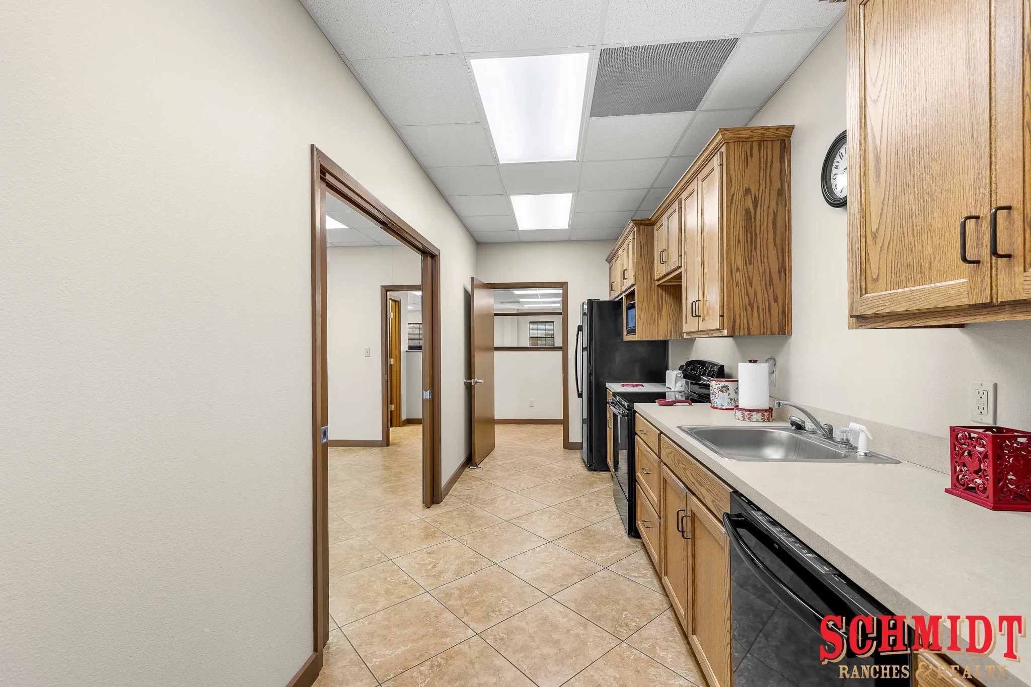 Galley kitchen with wood-finish cabinetry, black appliances, a stainless steel sink, and light-toned countertops